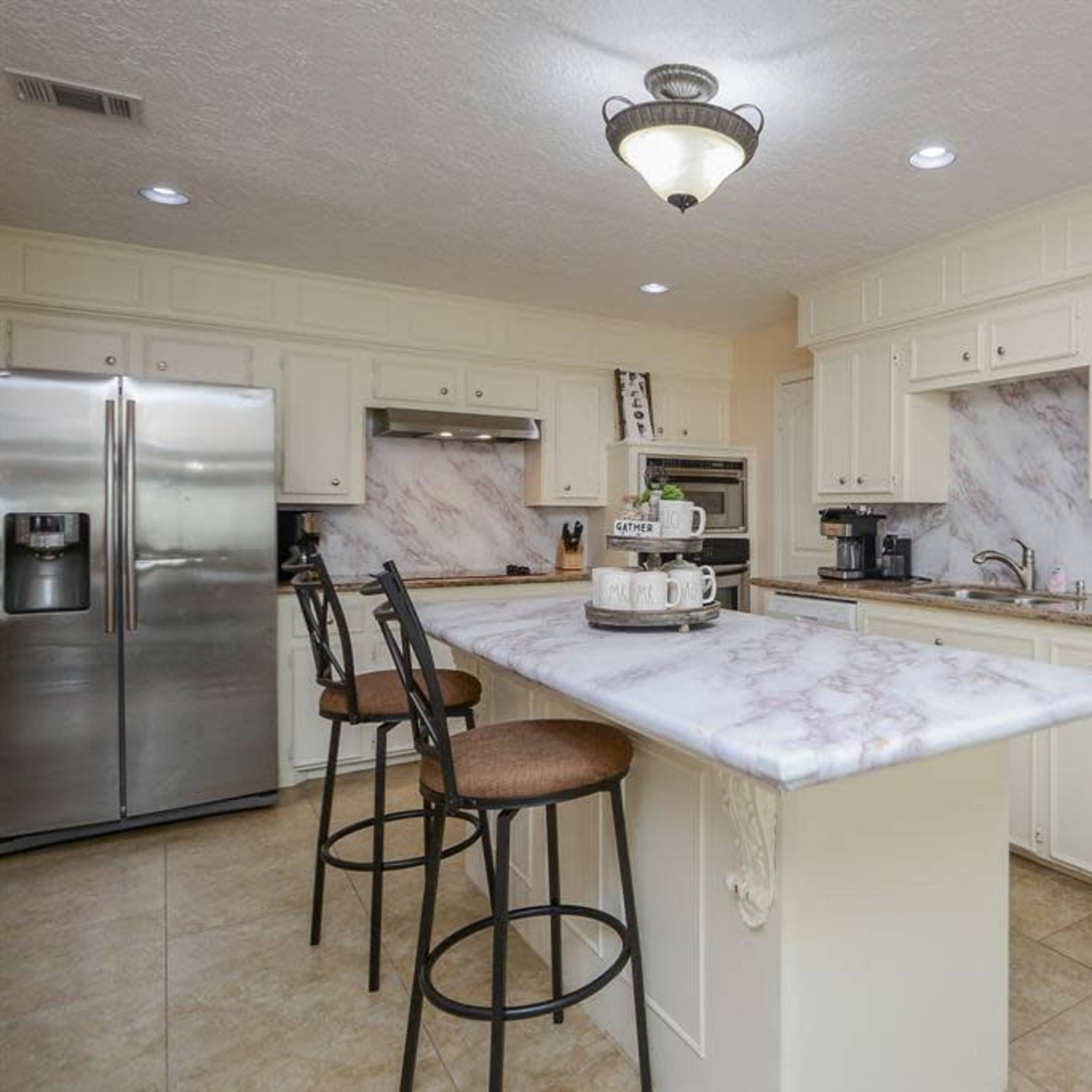 The kitchen features a marble-topped island with bar seating, white cabinets, and stainless steel appliances.