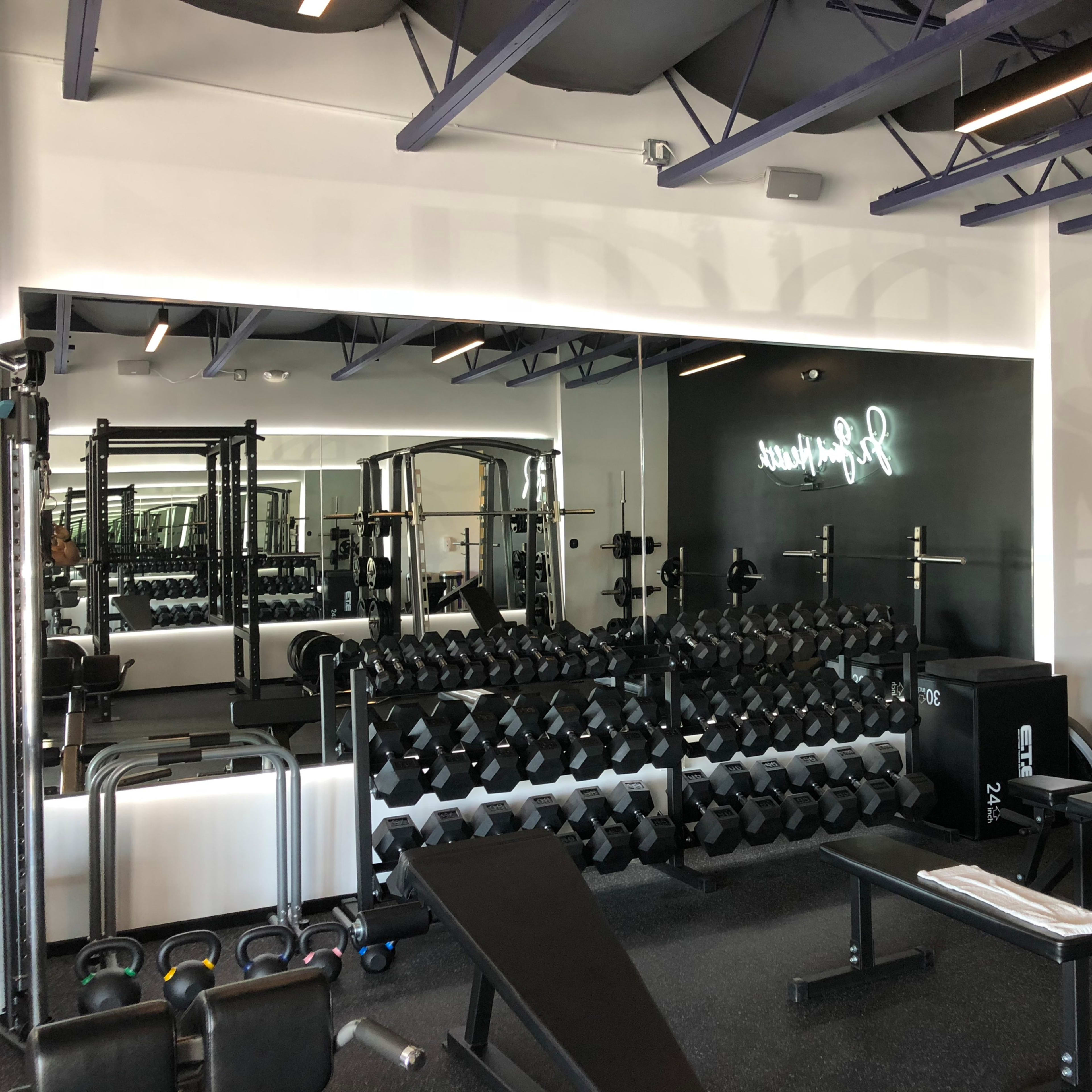 A modern gym interior with a weightlifting area featuring a rack of dumbbells, benches, and various exercise equipment.