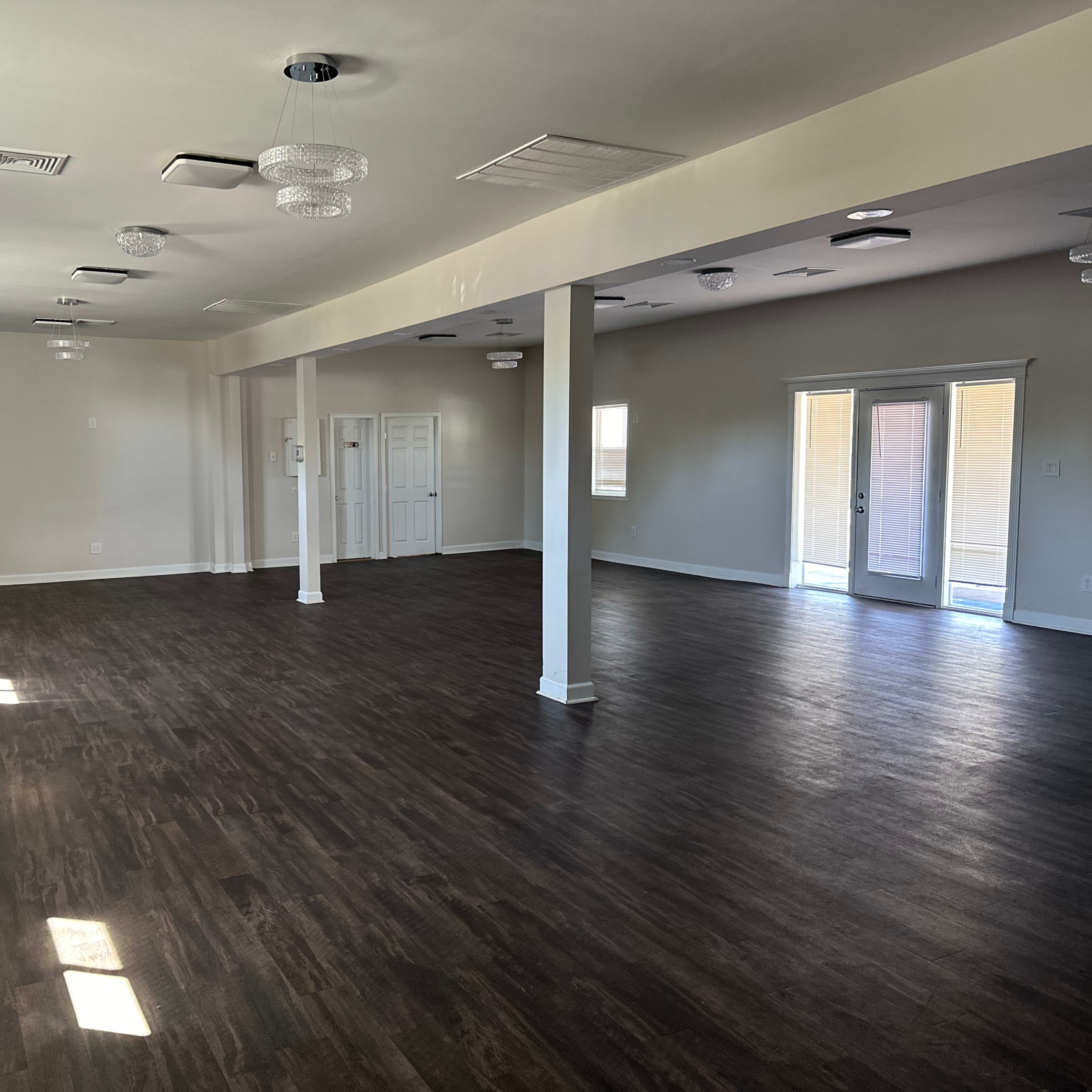An empty room with dark wooden flooring, white walls, and multiple light fixtures hanging from the ceiling.