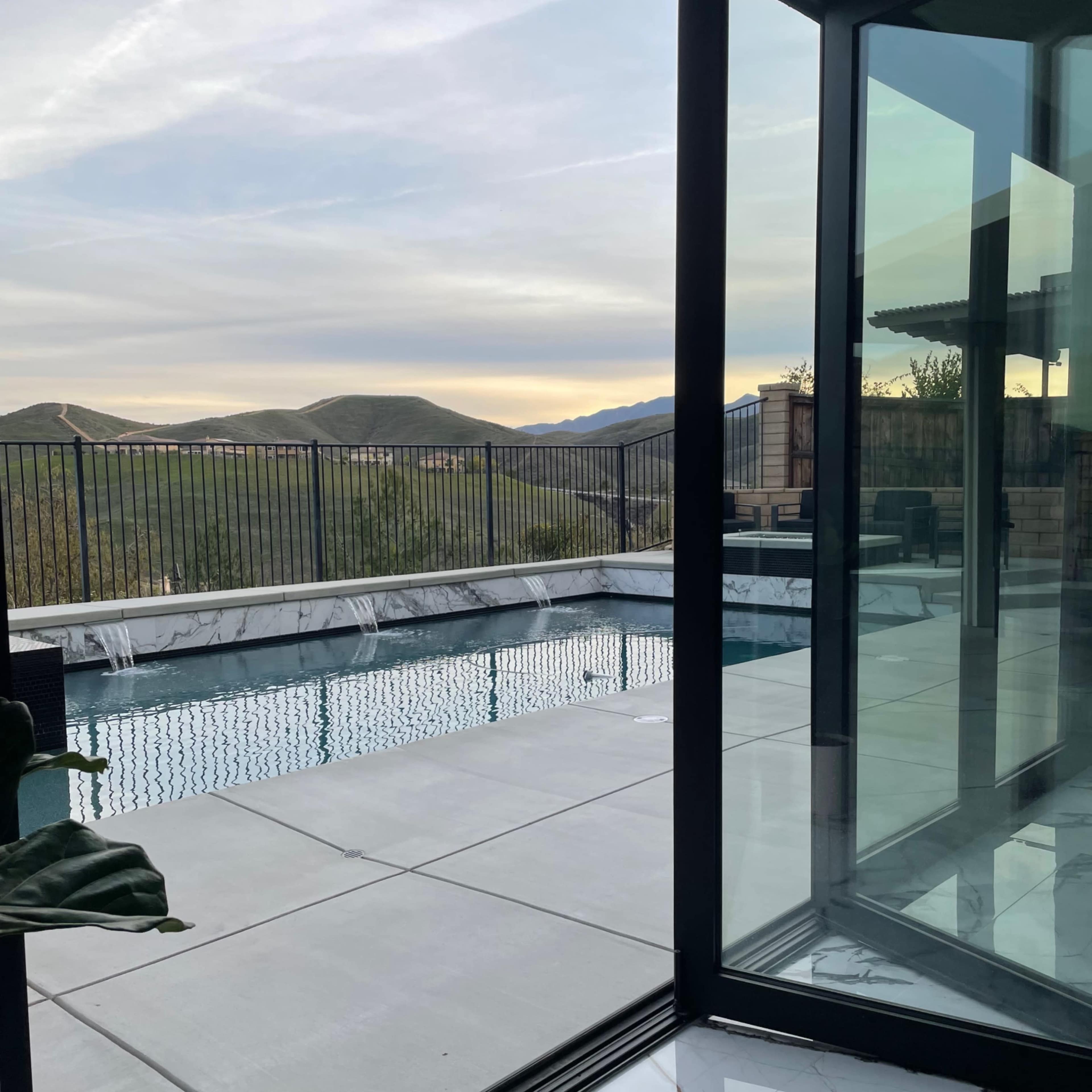 A modern indoor space with floor-to-ceiling glass walls overlooking a swimming pool and mountainous landscape.