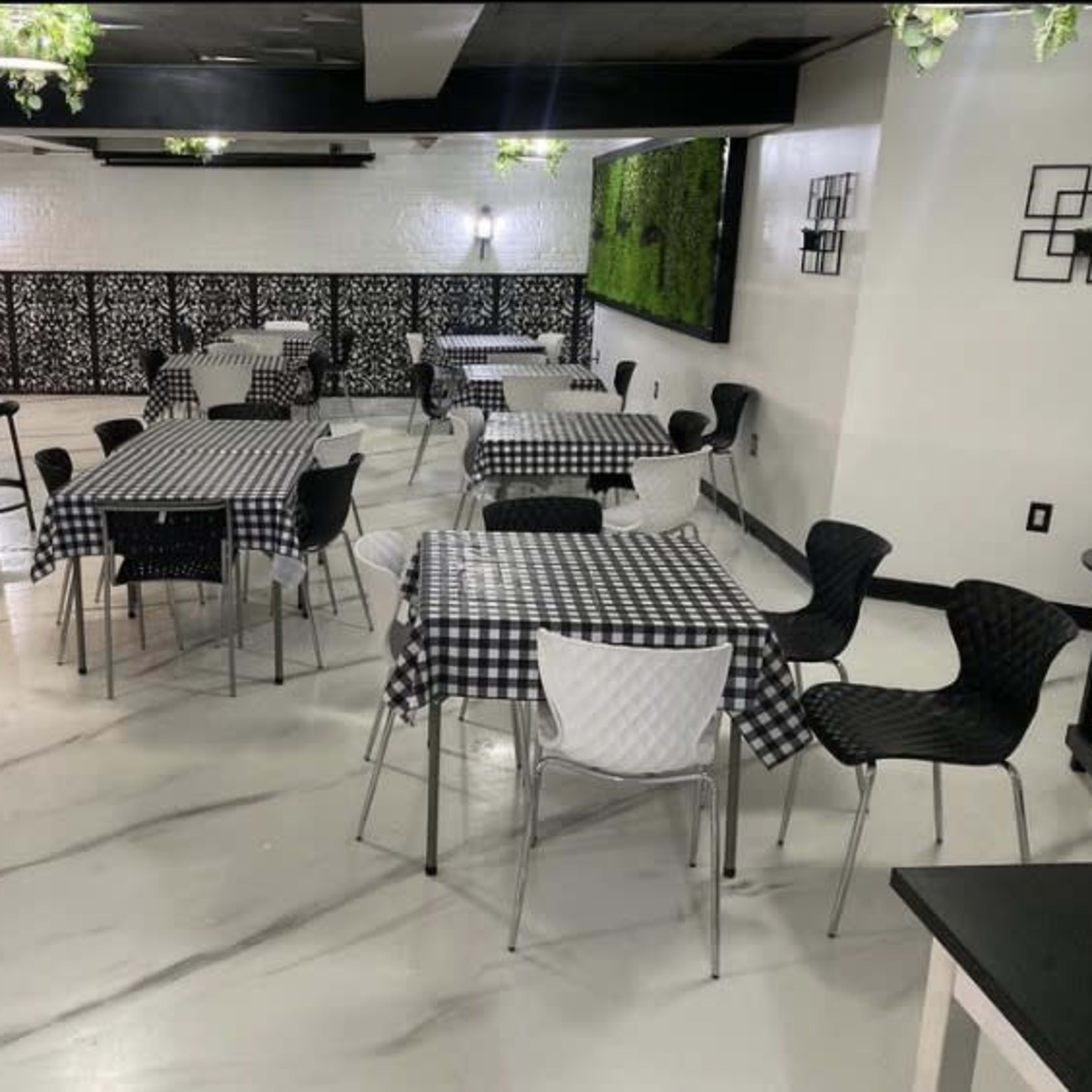 A restaurant interior with several tables covered in black and white checked tablecloths, surrounded by modern seating and greenery decor on the walls.