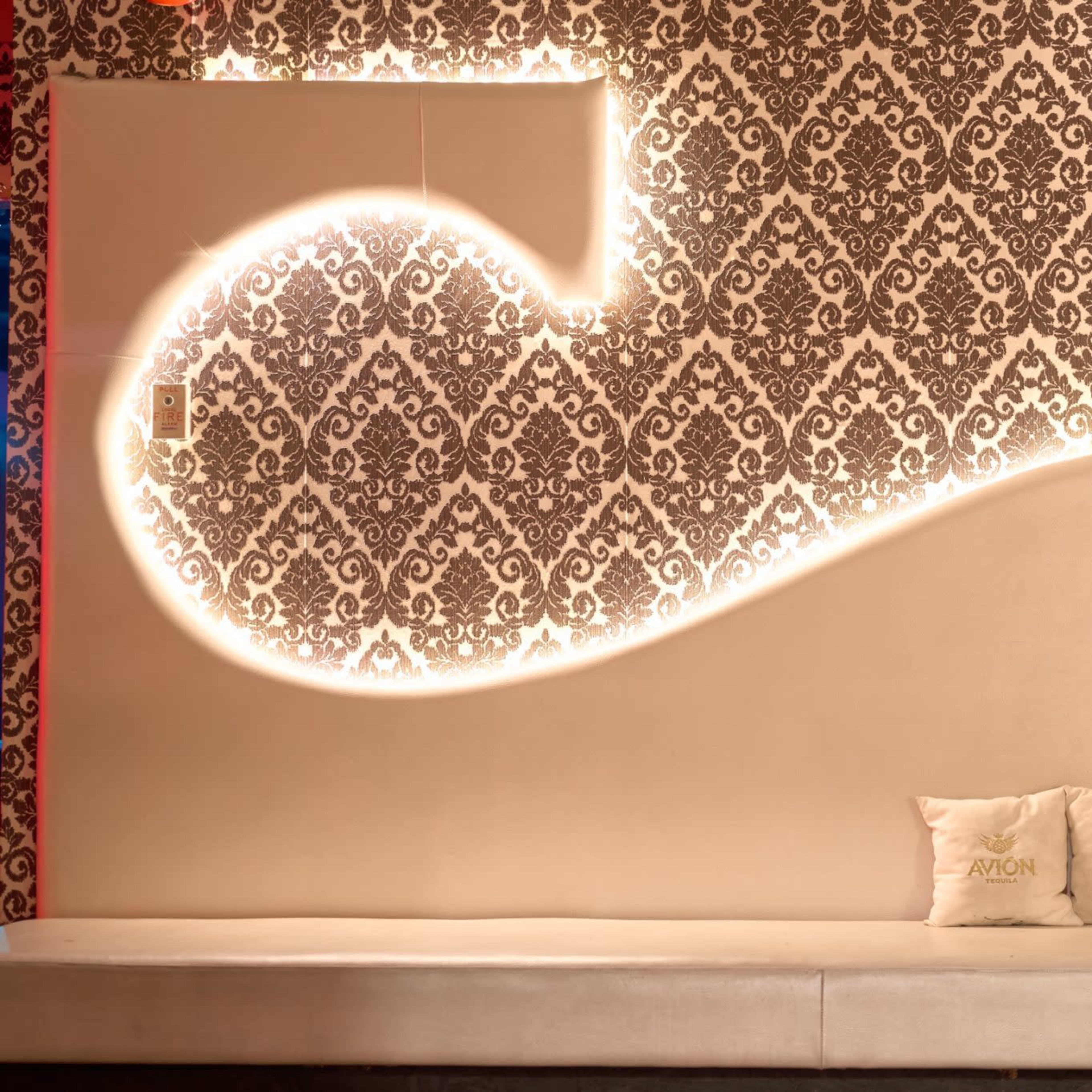 A modern seating area with a white sofa against a decorative wall featuring an intricate pattern and softly illuminated accents.