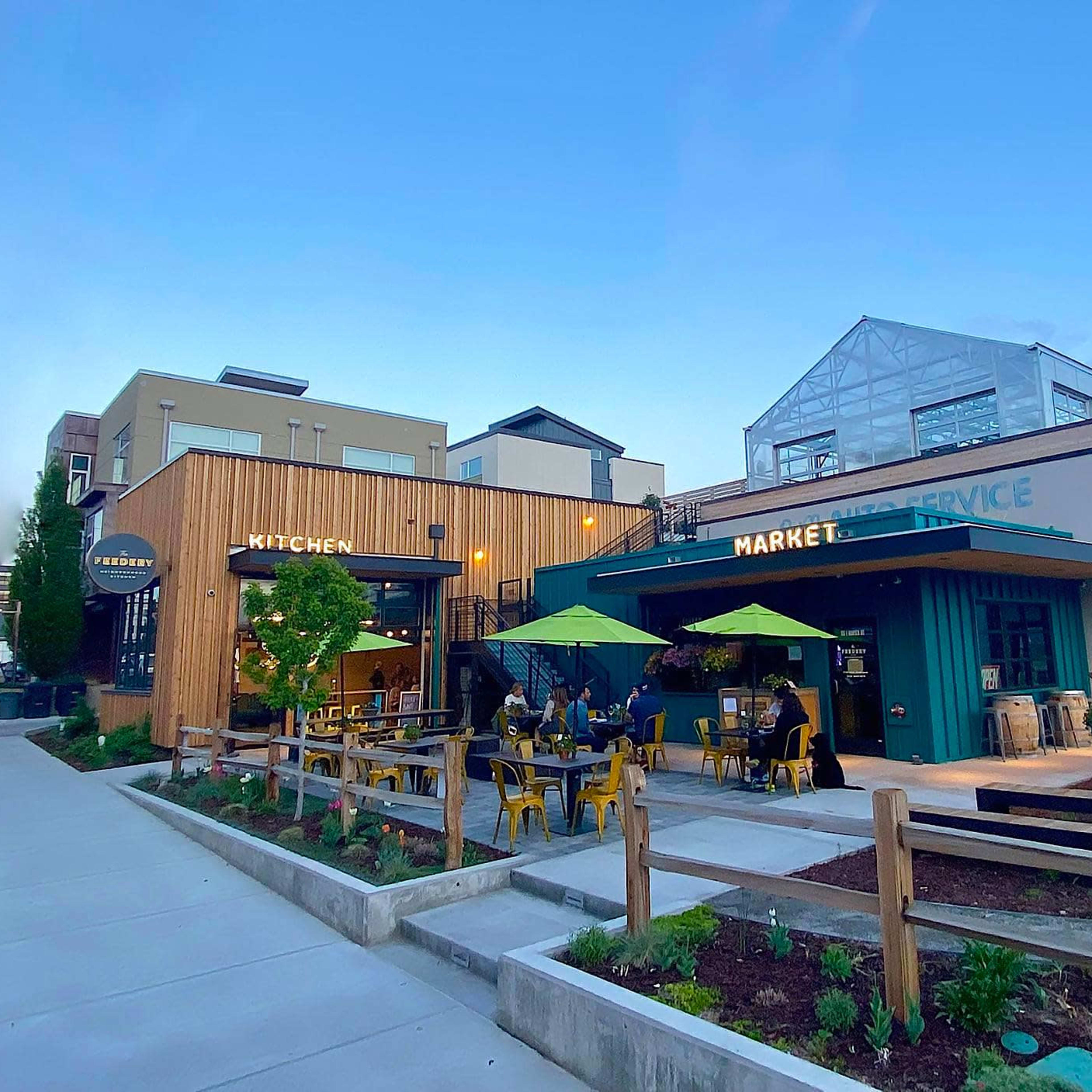 A modern building complex featuring a kitchen and market area with outdoor seating and green umbrellas.