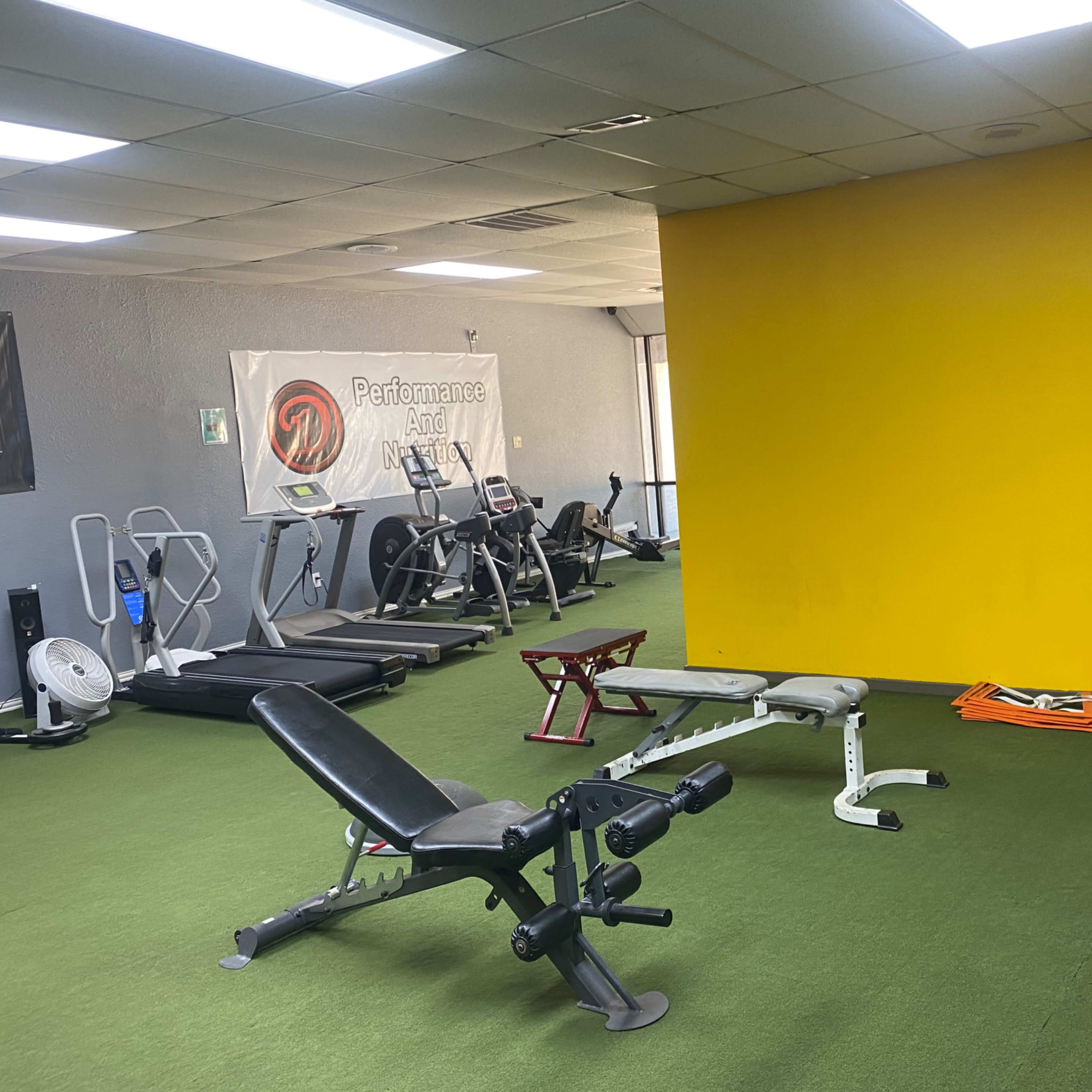 A gym interior with various exercise equipment, green flooring, and a yellow wall in the background.