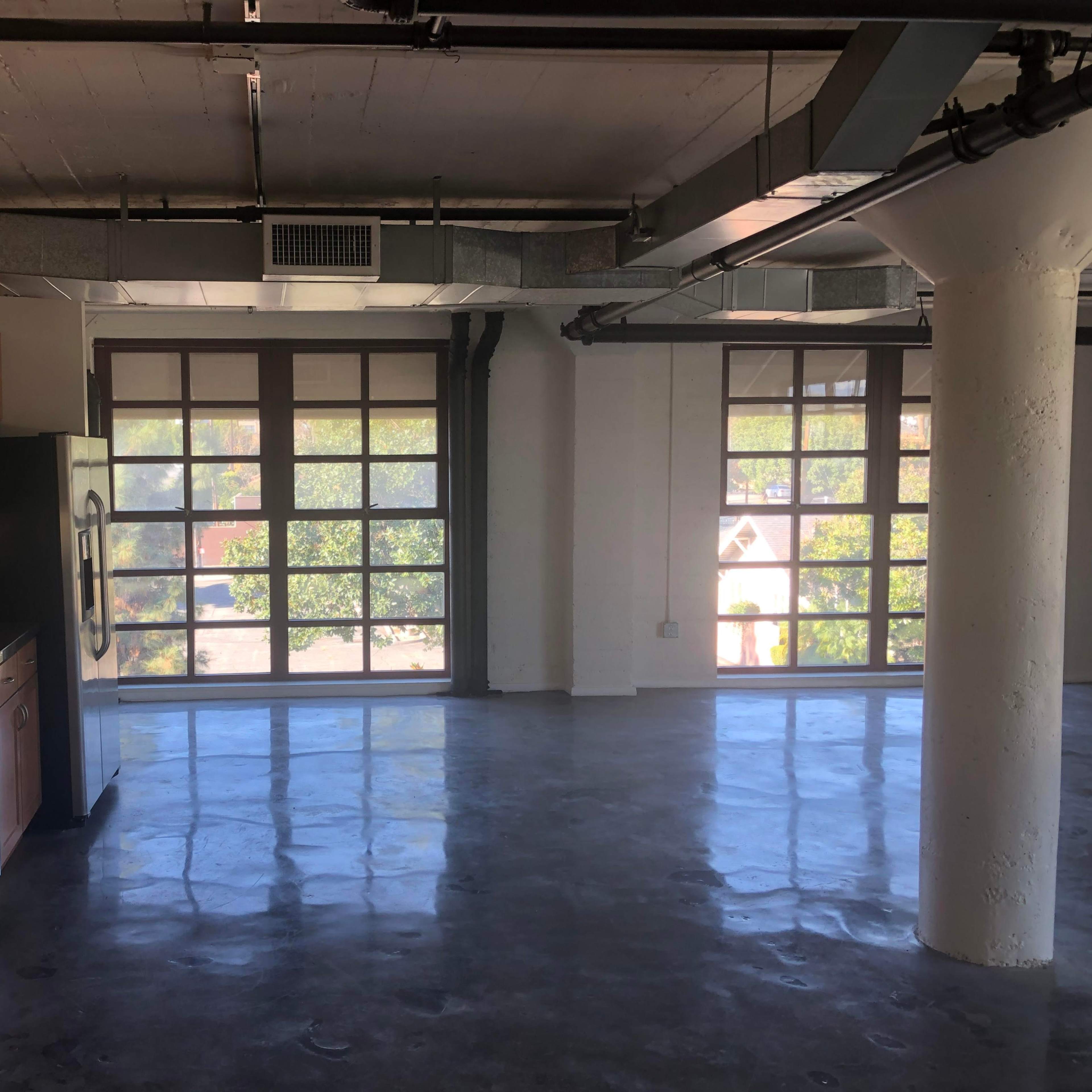 A spacious industrial kitchen area with wooden cabinets and a countertop, overlooking large windows in a modern apartment.