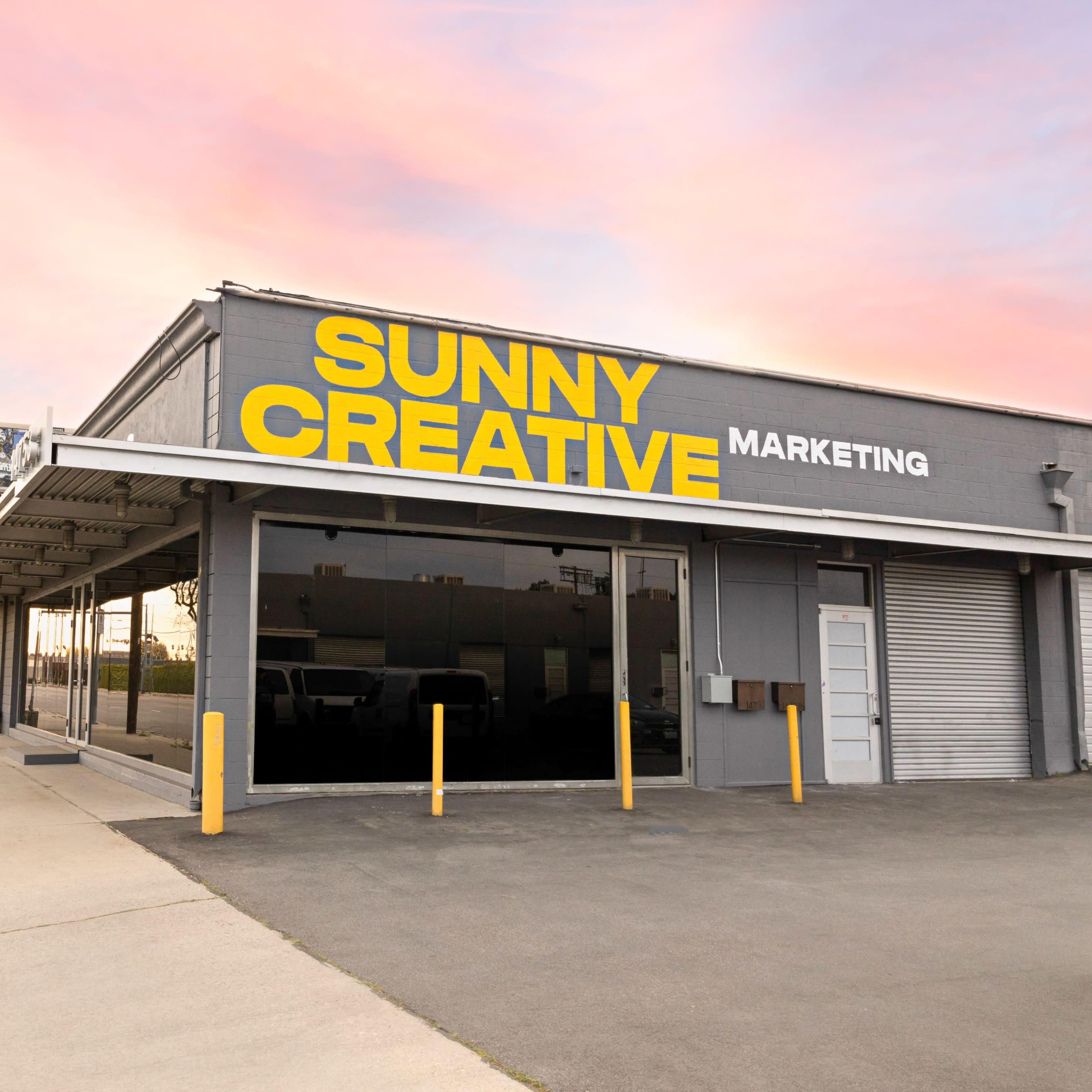 A building with large yellow signage reading "SUNNY CREATIVE MARKETING" is situated along a street lined with utility poles and a clear sky in the background.
