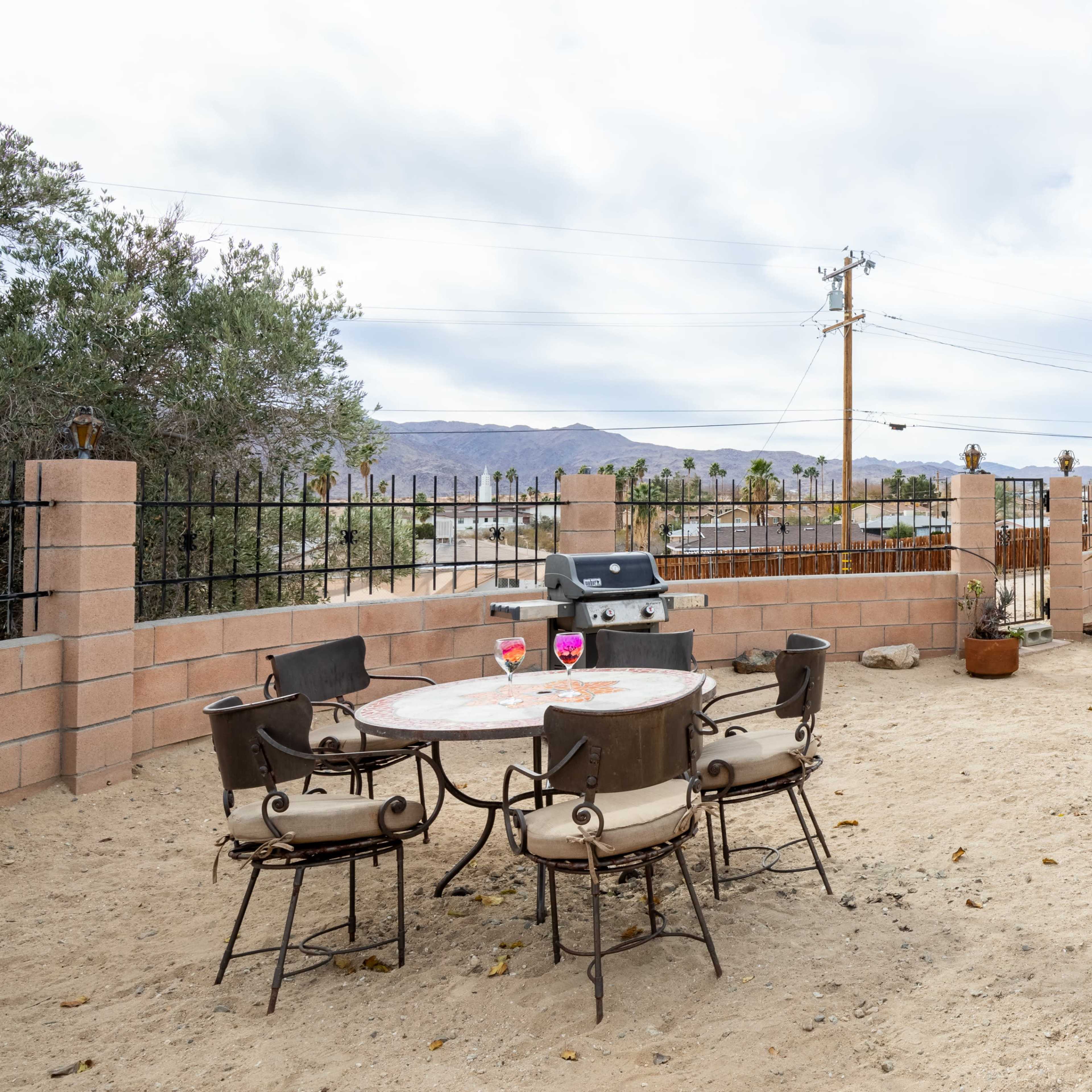 A patio area with several tables and chairs, a grill, and a desert landscape in the background.