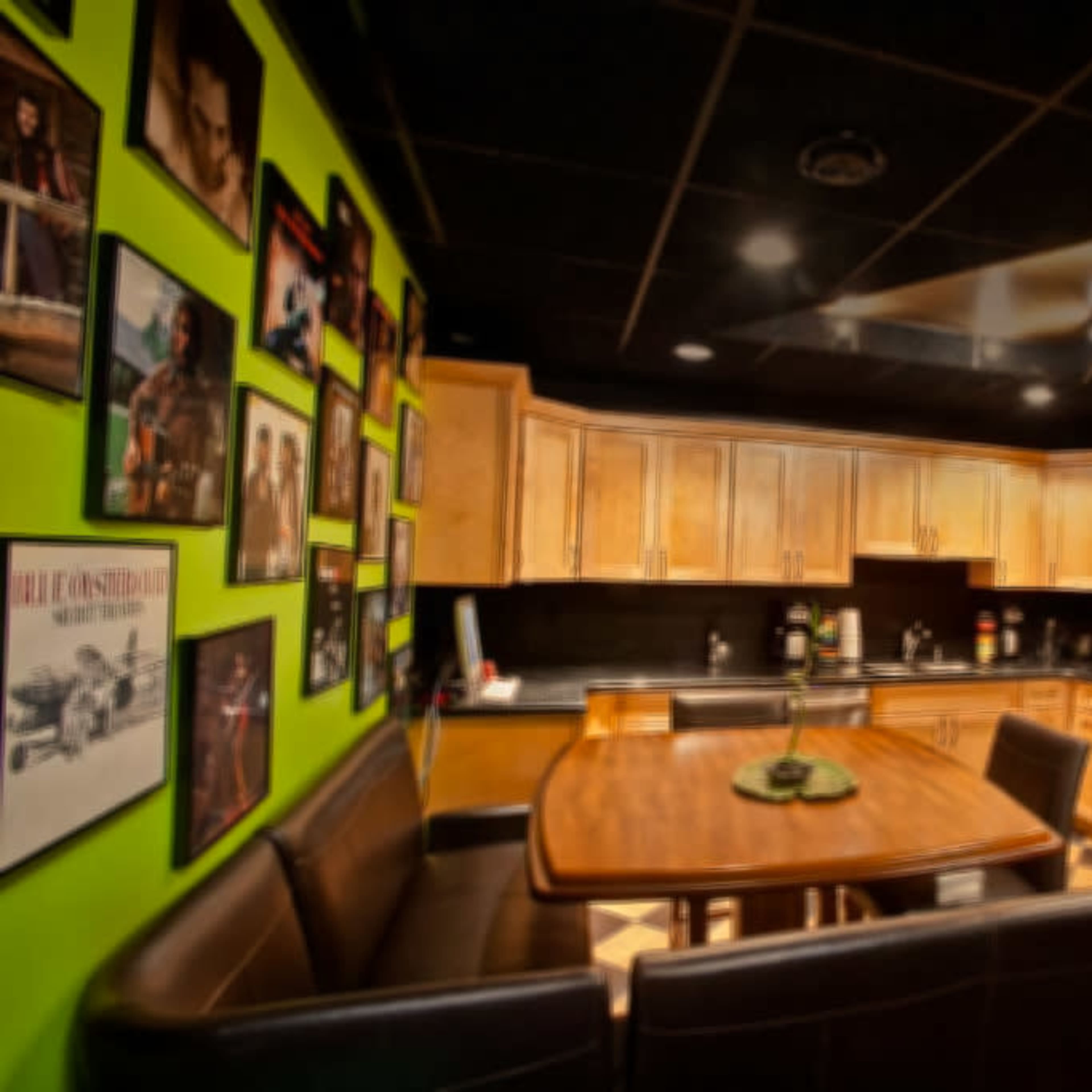 A modern kitchen with wooden cabinets, stainless steel appliances, and a black countertop, featuring a dining table surrounded by leather chairs.