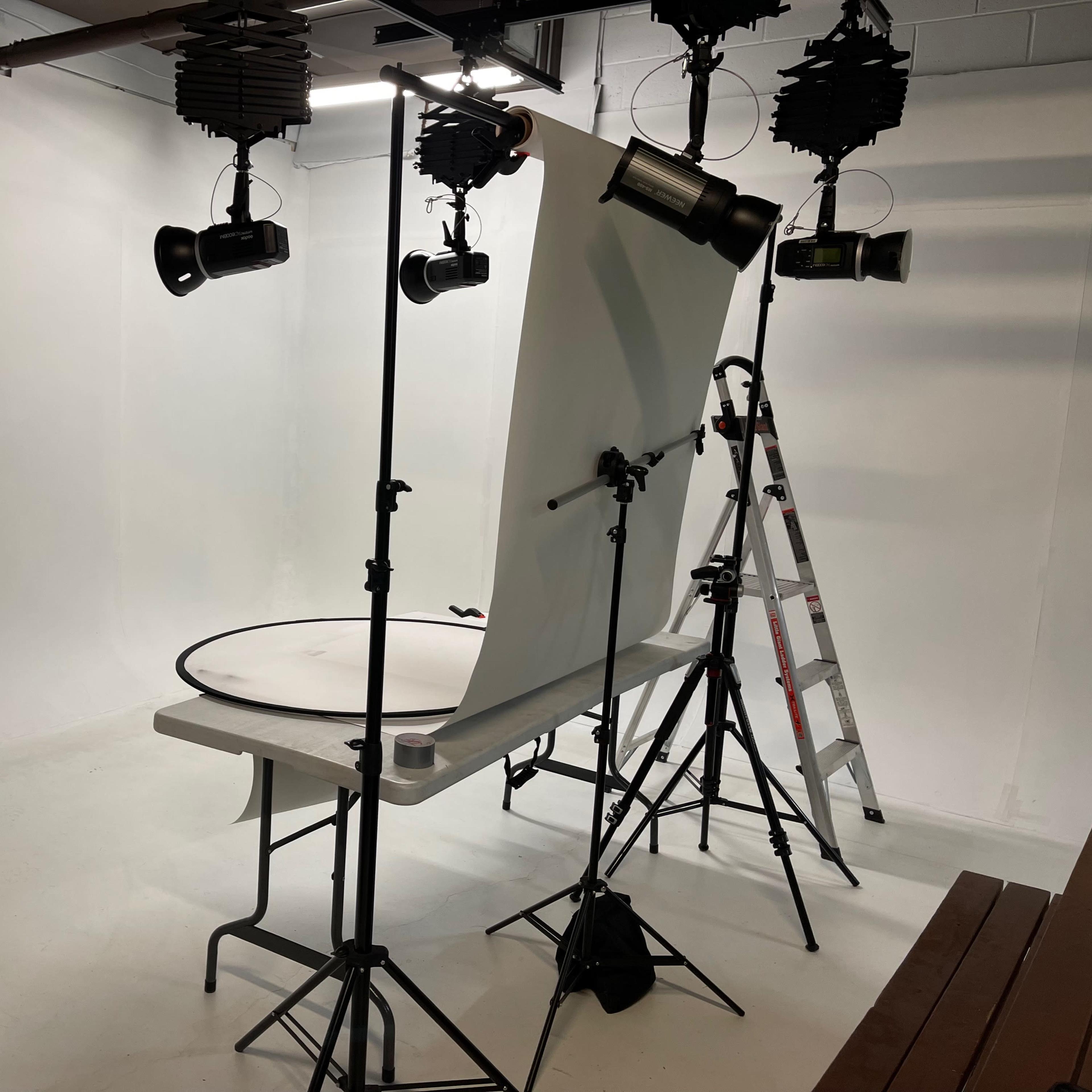 A photography studio setup with a white backdrop, a circular table, and various lighting equipment.