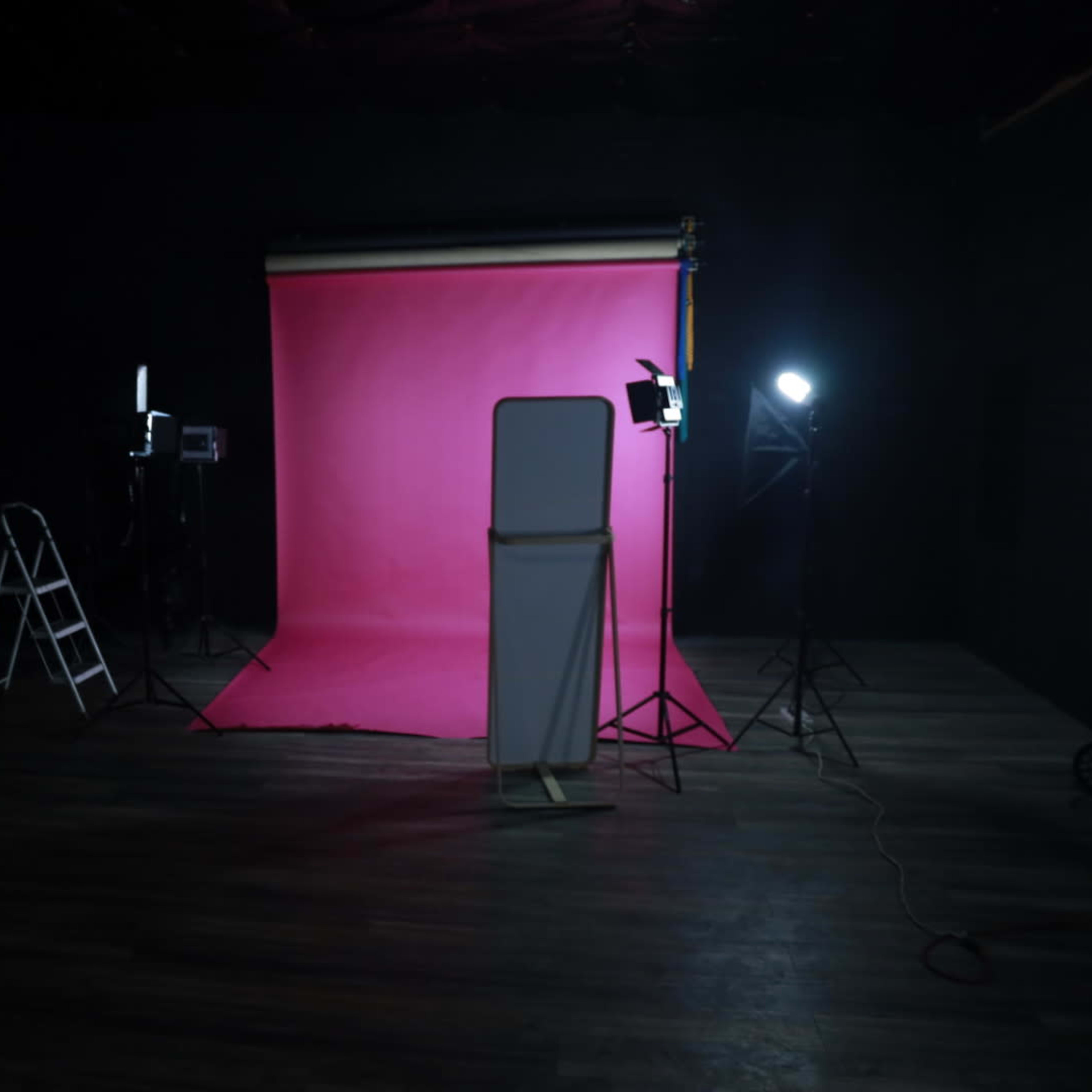 A photography studio with a pink backdrop, lighting equipment, and a ladder positioned nearby.