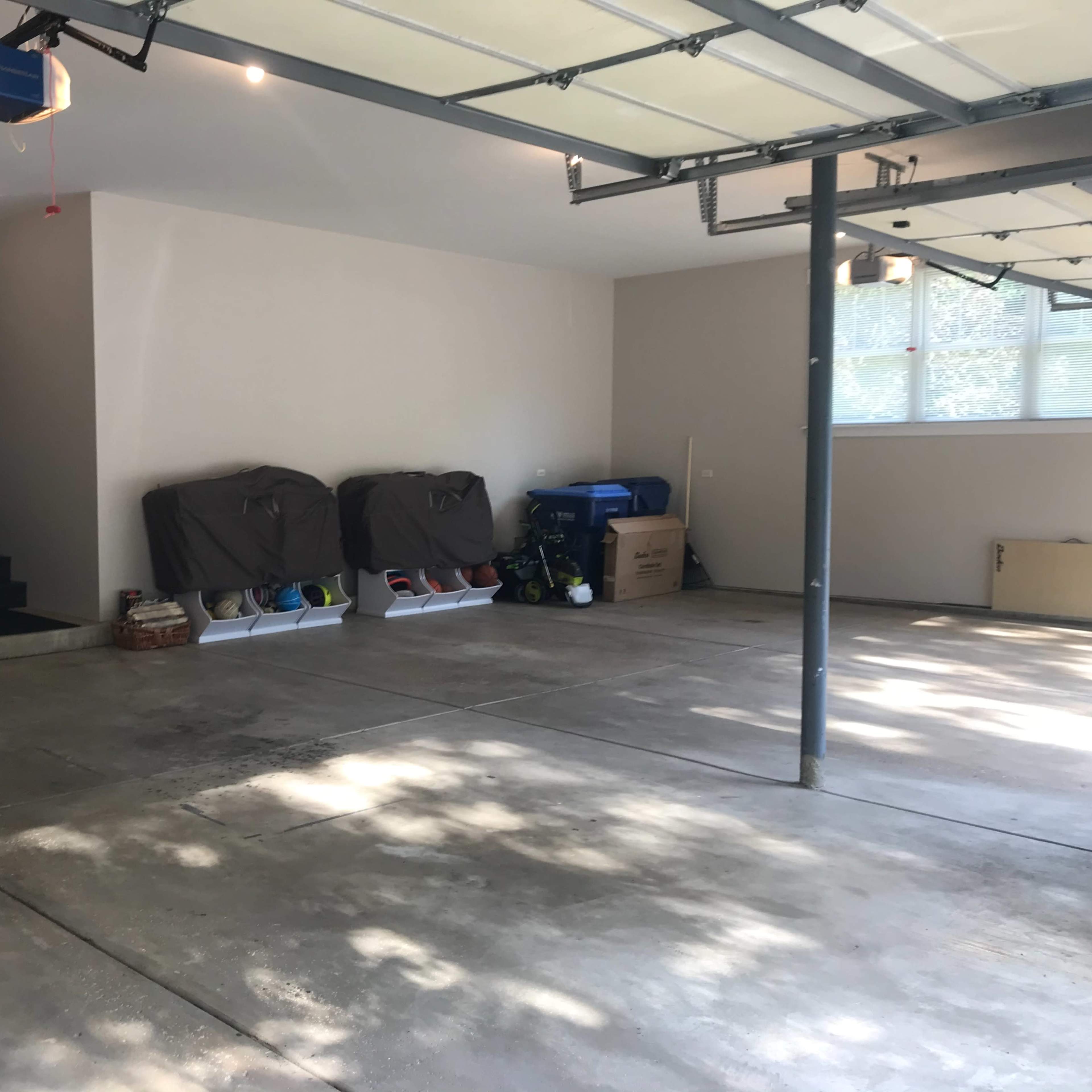 A spacious, empty garage with a staircase leading to an upper level and storage bins covered with fabric on one side.