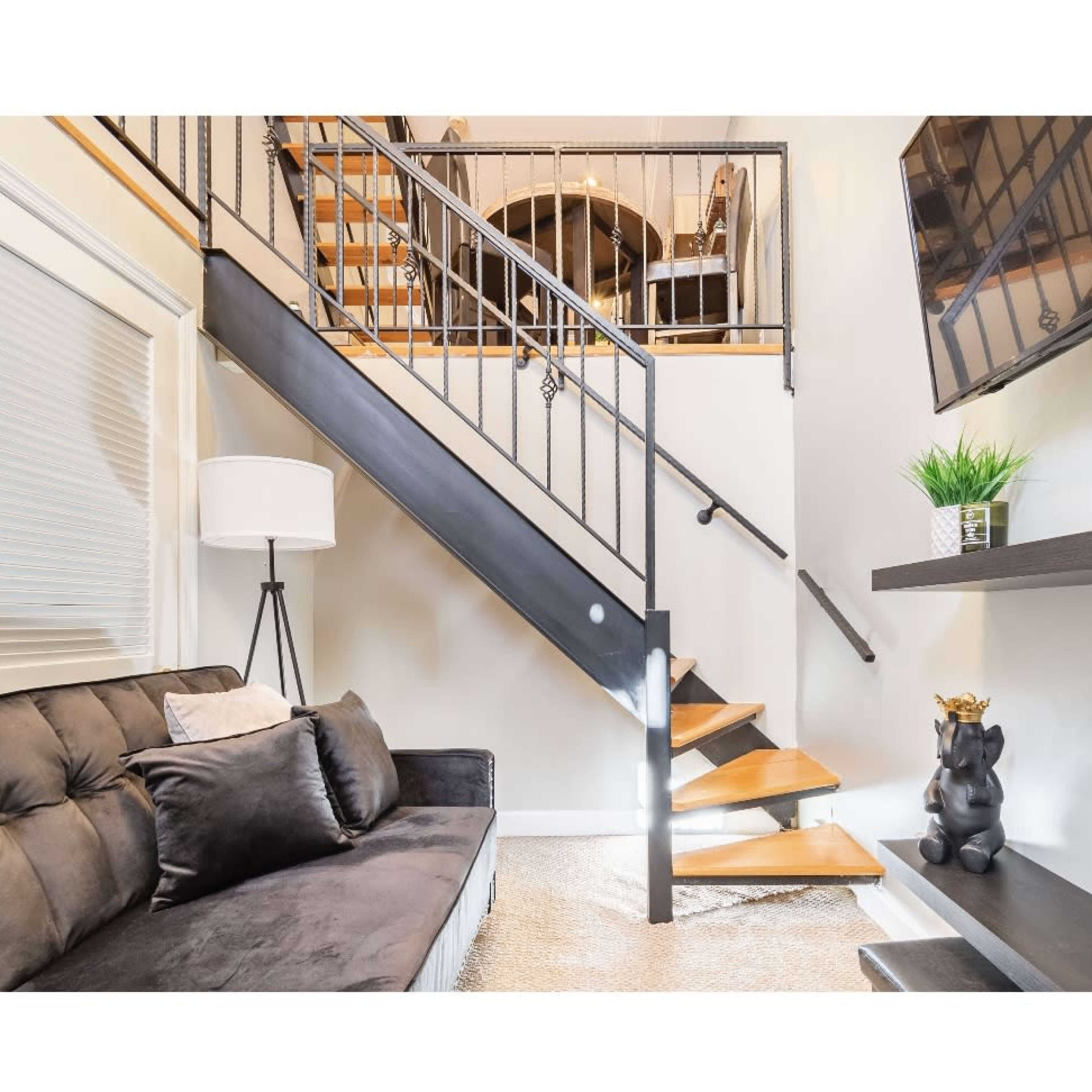 A modern living space with a black sofa, a staircase leading to an upper level, and a television mounted on the wall.