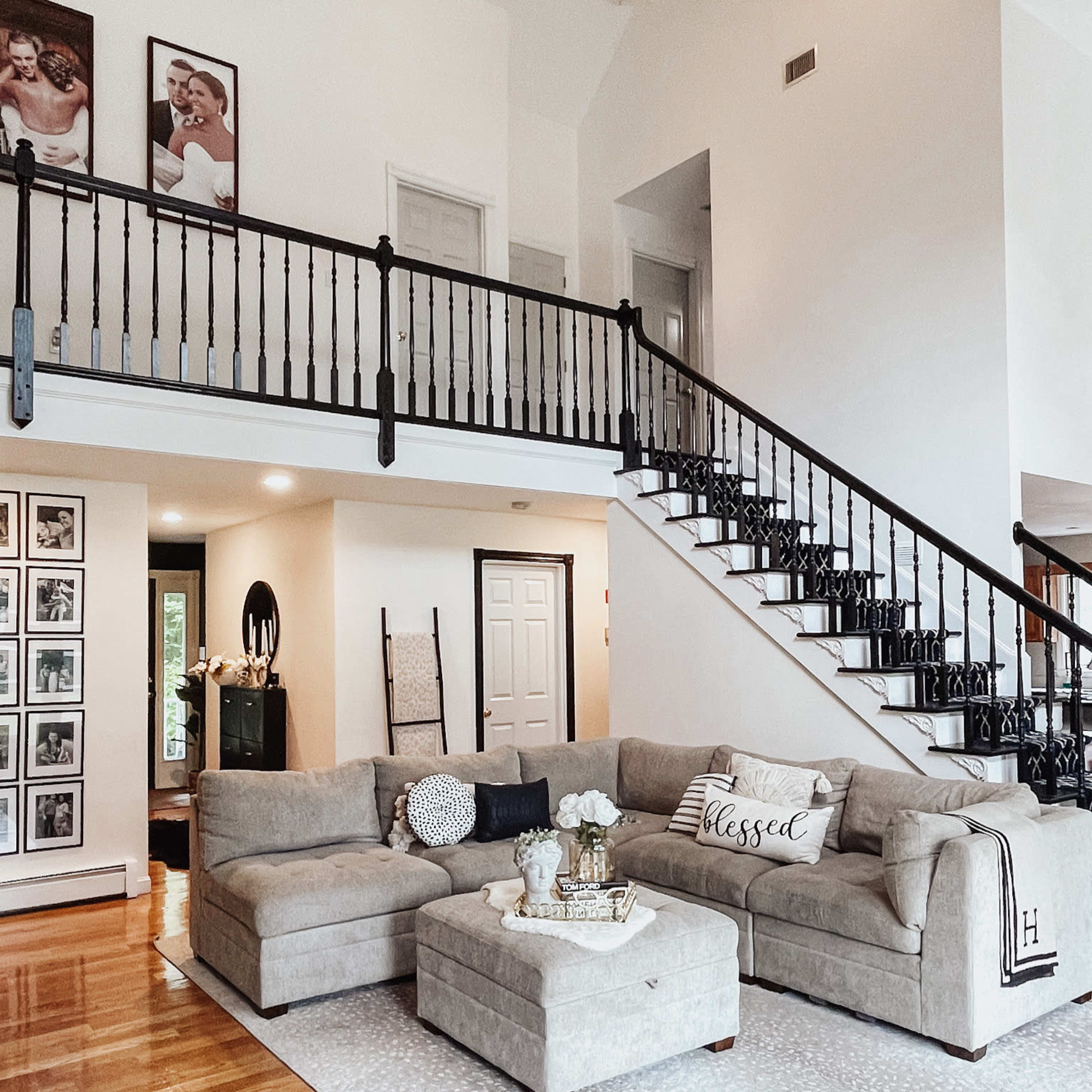 A spacious living room with a large sectional sofa, a coffee table, and a staircase leading to an upper level, all set against a bright, neutral color palette.