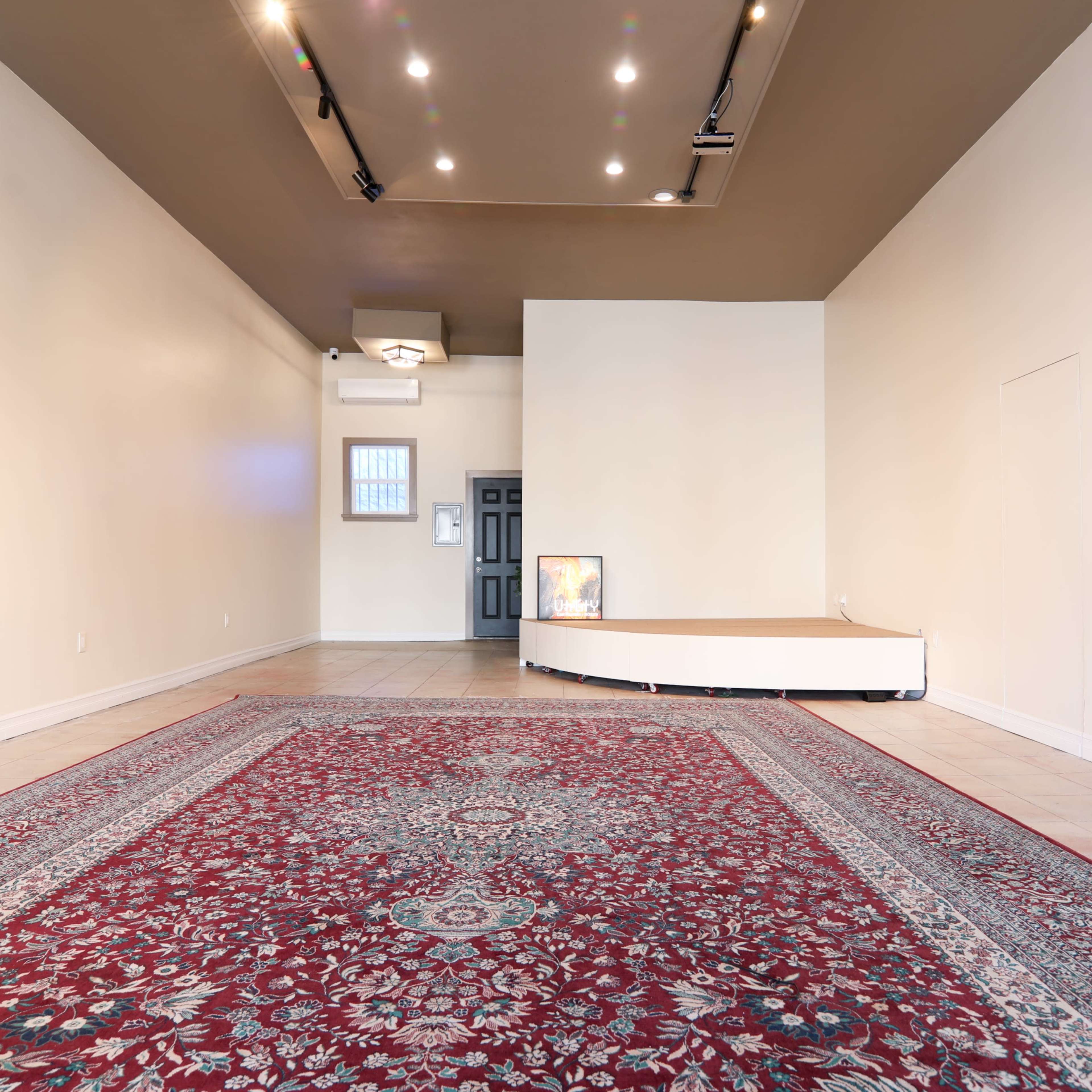 An empty room with a large rug, a small raised platform, and a door at the far end.