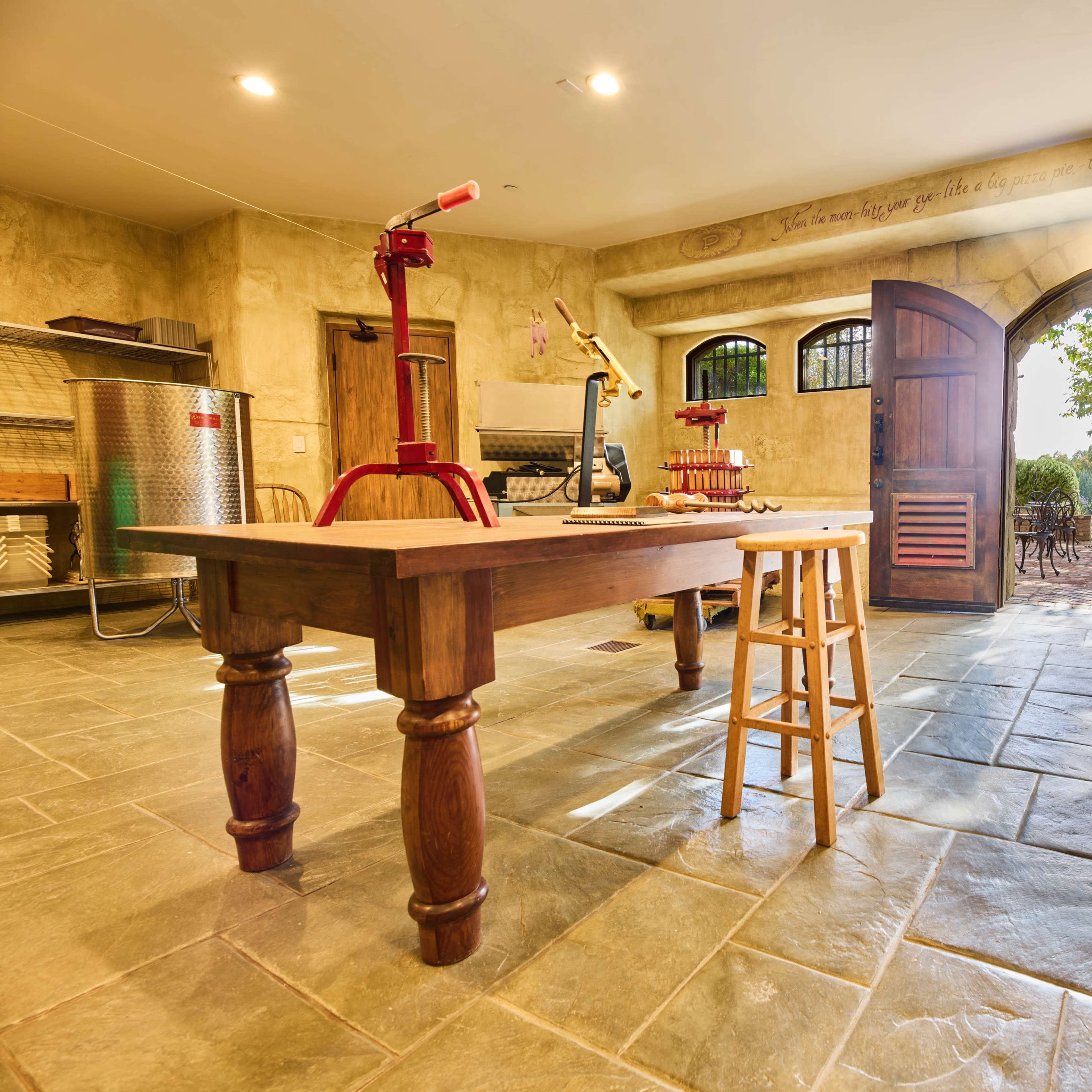A rustic kitchen with a wooden table, a stool, and double doors leading to an outdoor patio area.