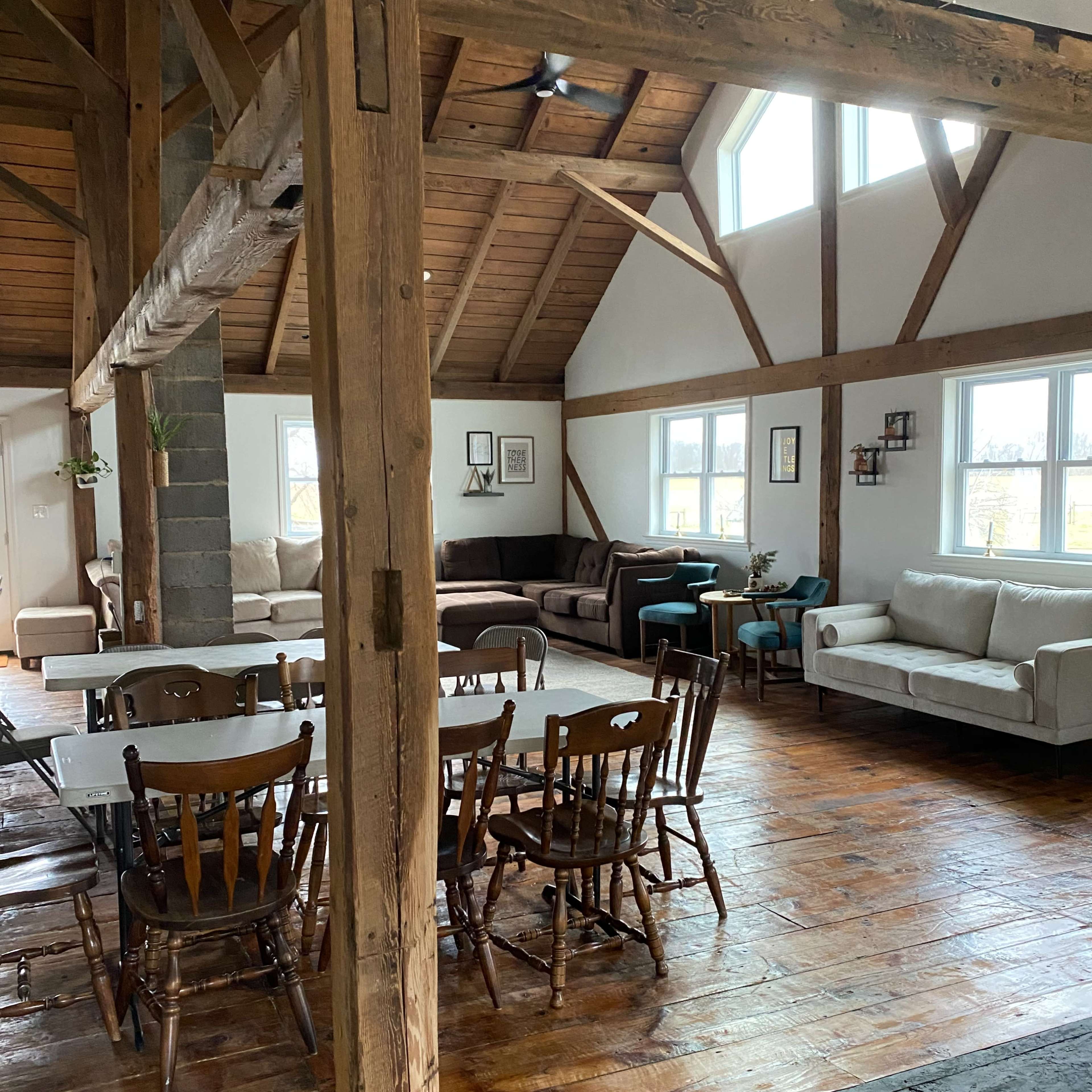 A spacious open-plan living area with wooden beams, a dining table surrounded by chairs, and various seating arrangements including couches.