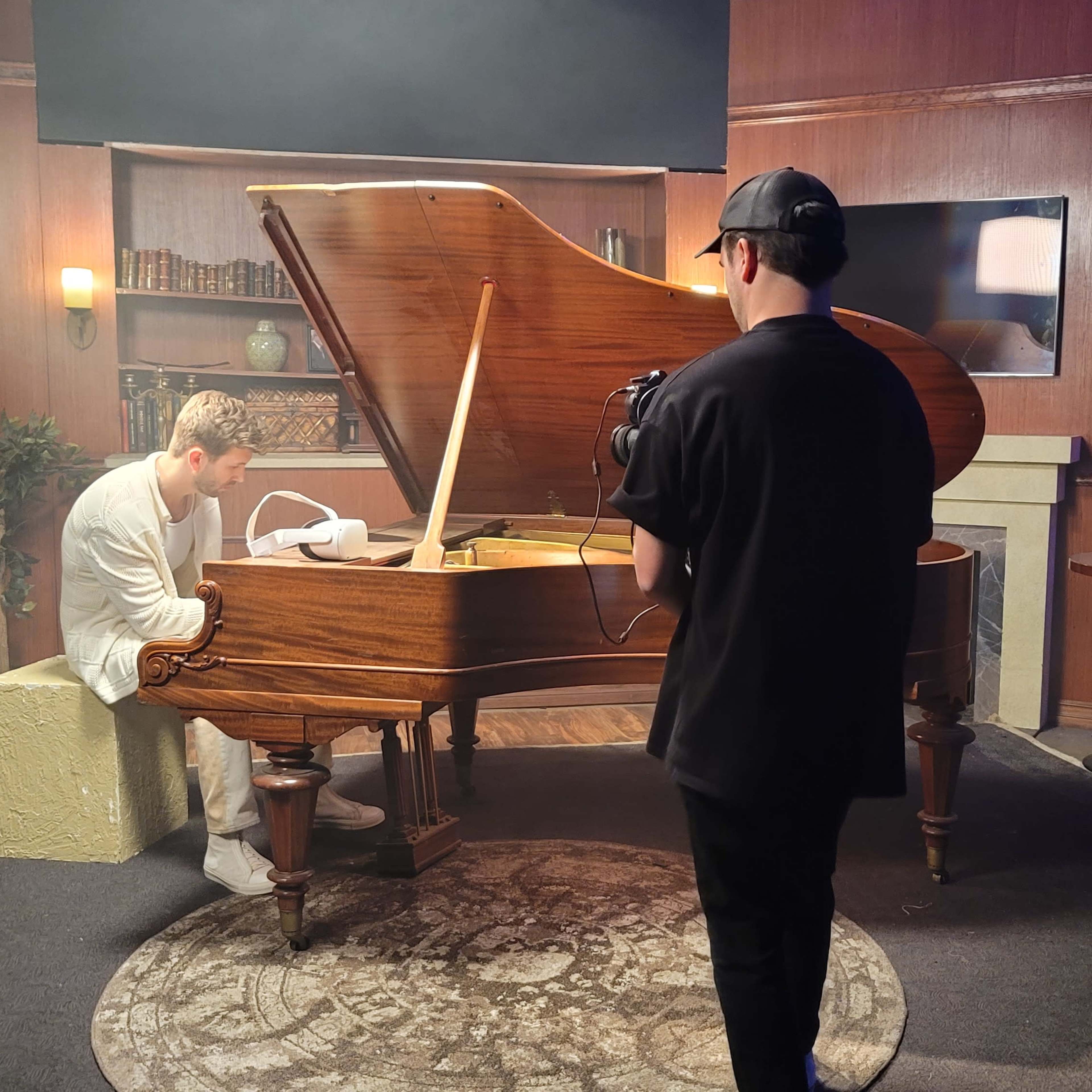 A musician plays a grand piano while a person records the performance with a camera.