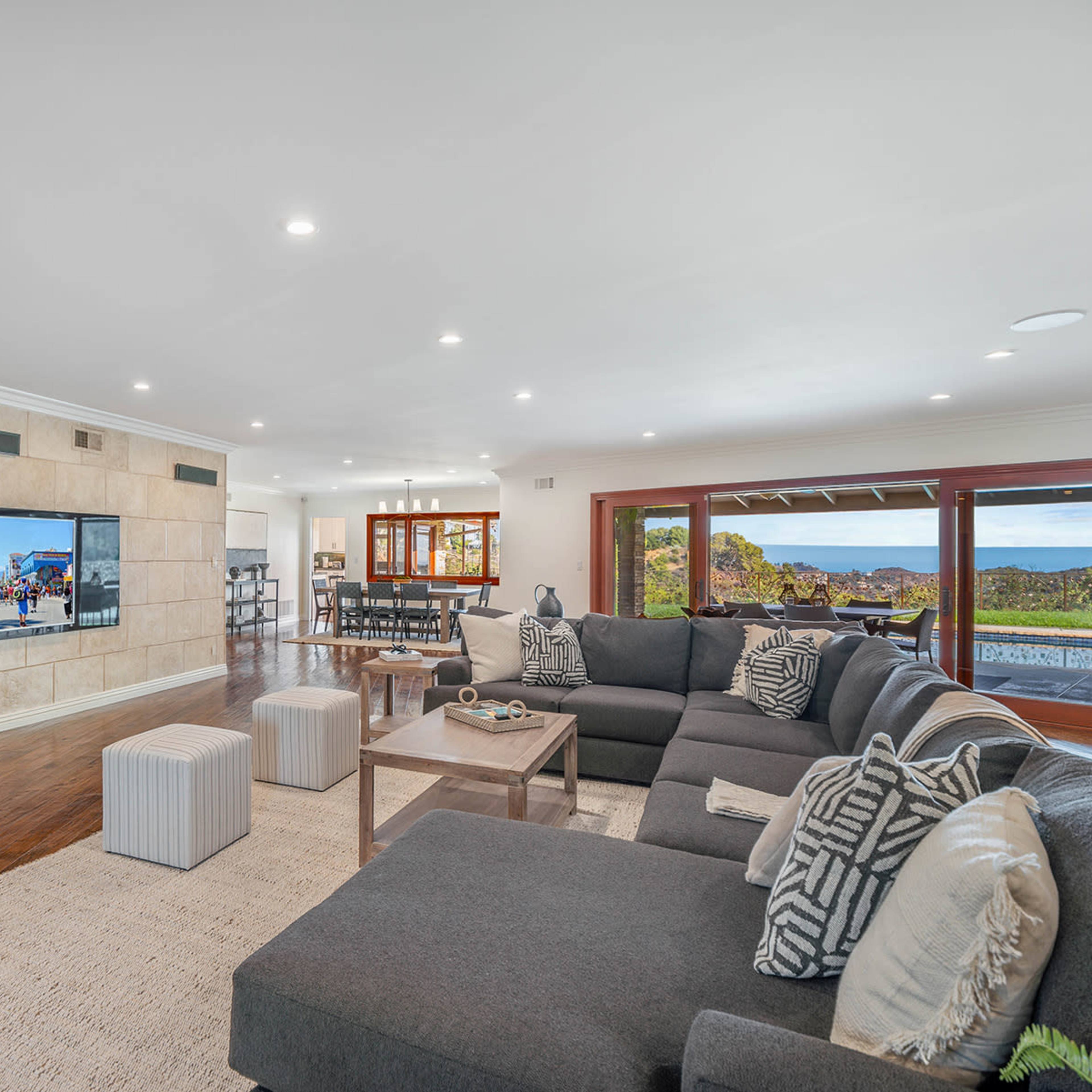 A spacious living room with a large sectional sofa, a coffee table, and a mounted television displaying a scenic view.