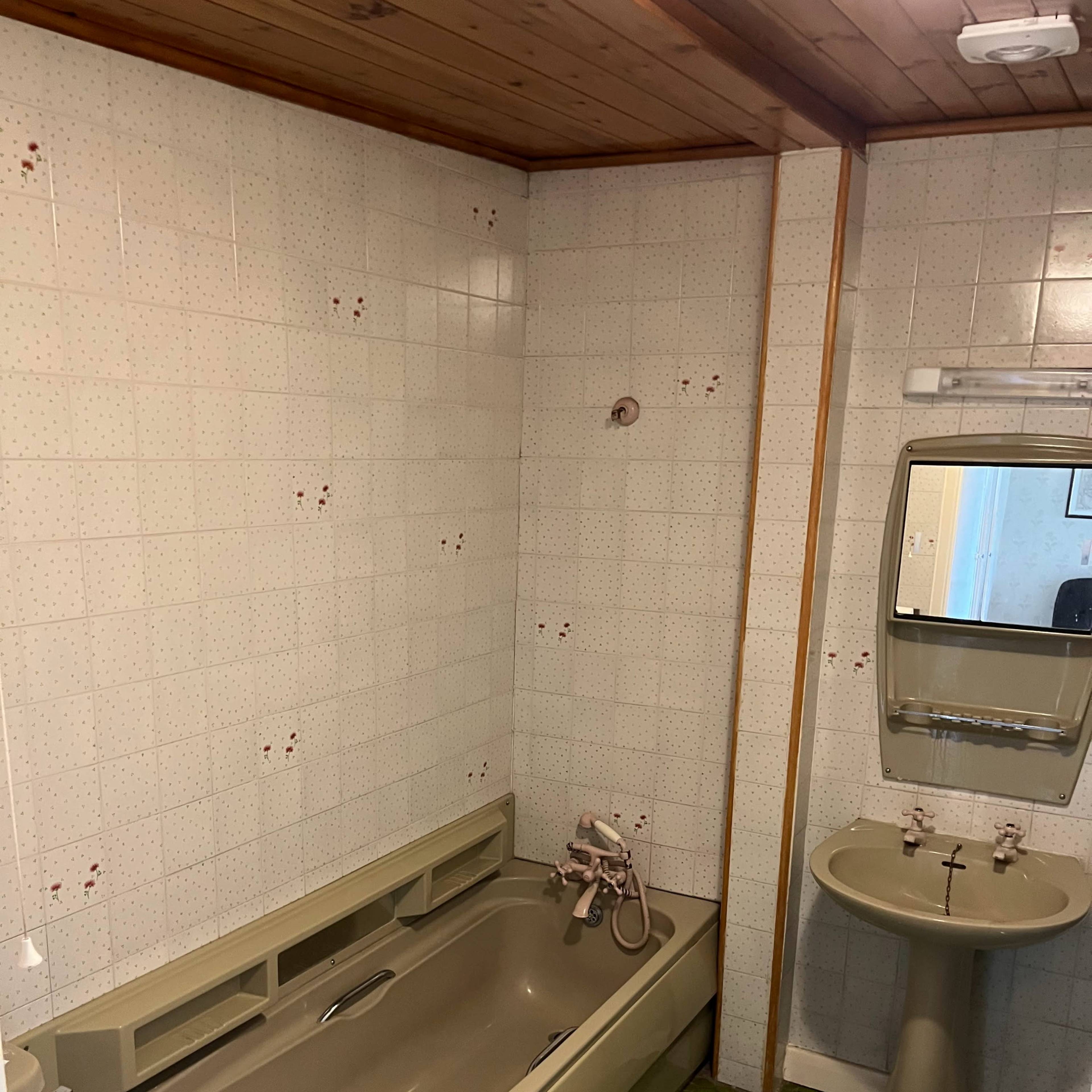 A small bathroom featuring a bathtub, sink, and tiled walls with a green patterned floor.