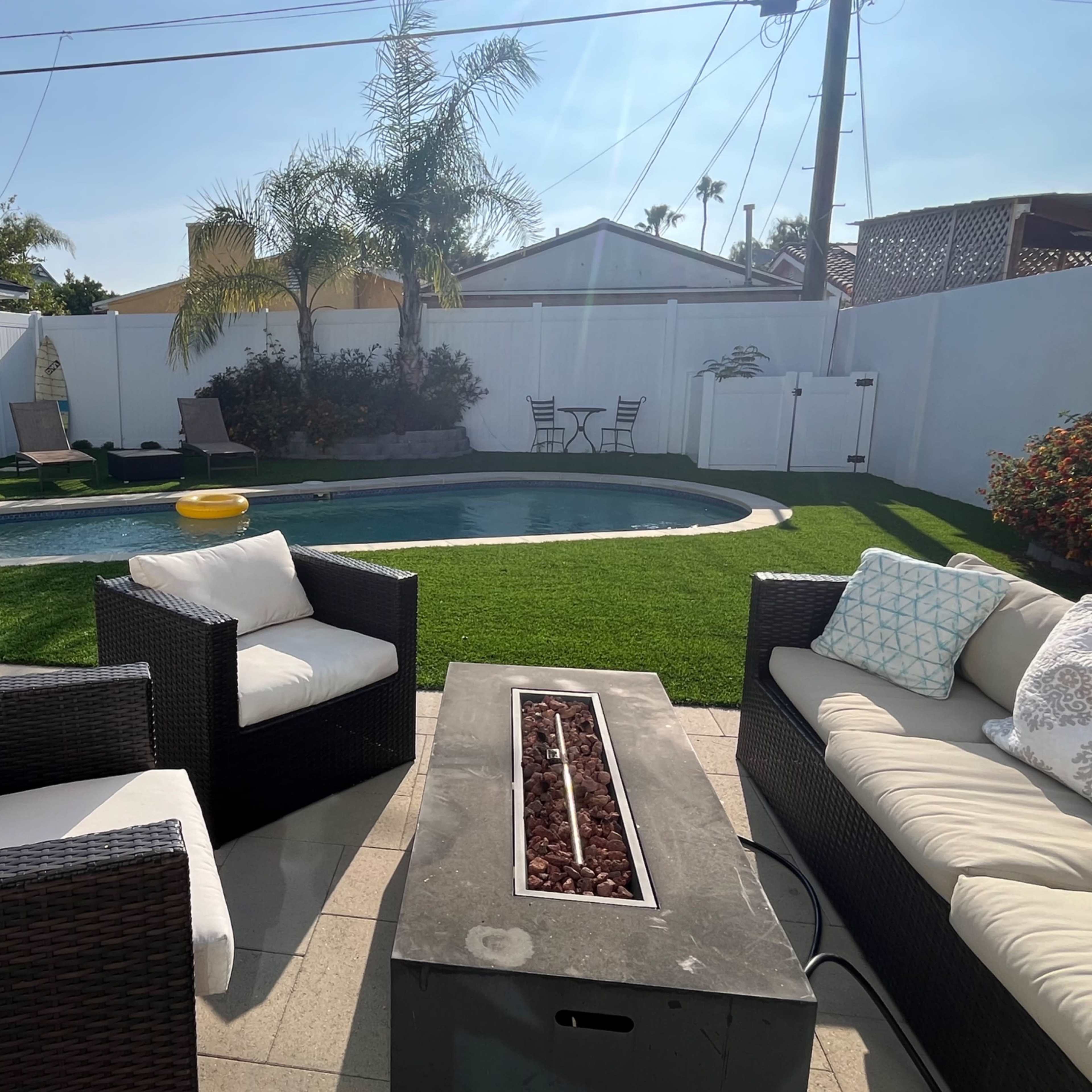 A backyard with a swimming pool, lounge chairs, and outdoor seating arranged around a fire pit on a patio.