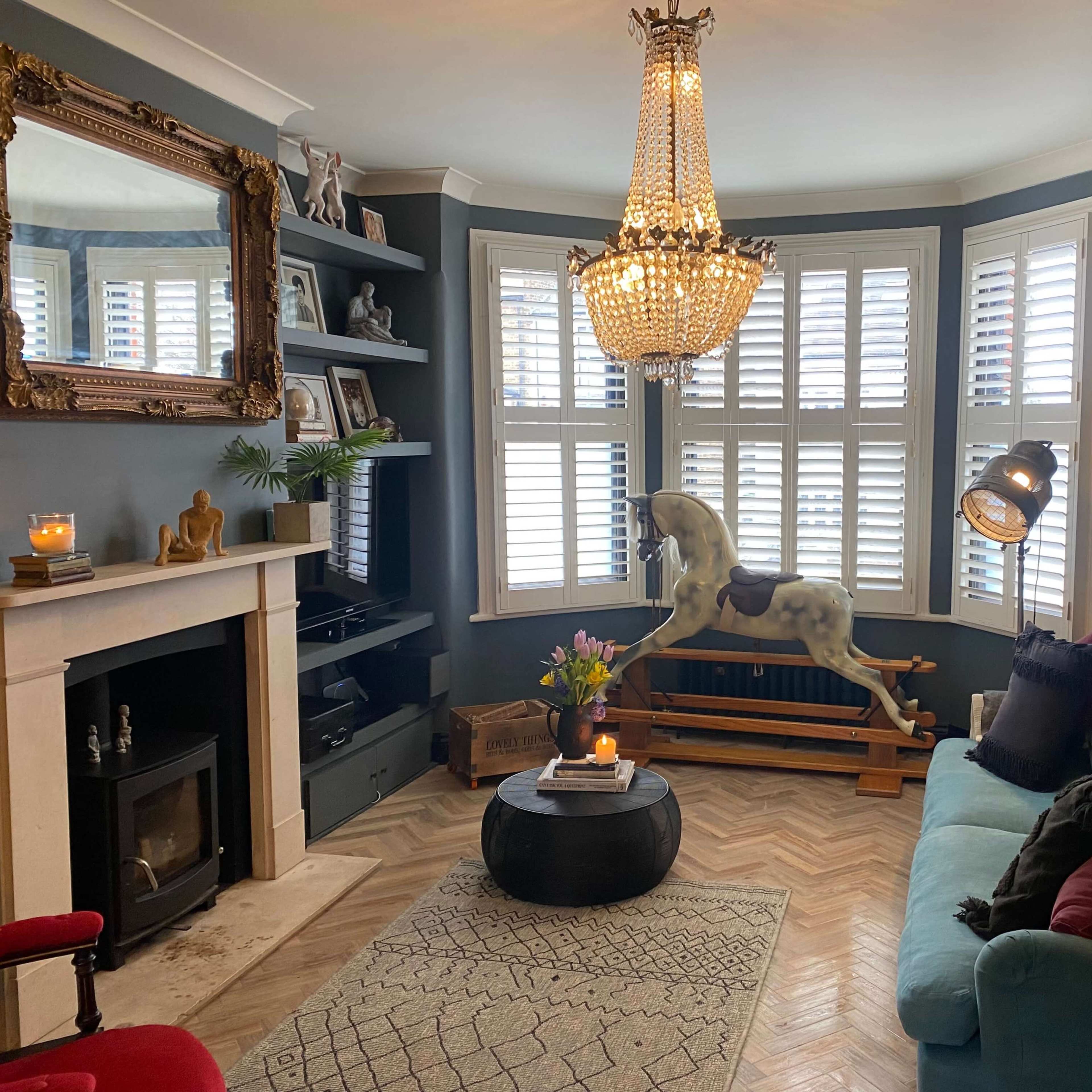 A cozy living room featuring a blue sofa, a large chandelier, a wooden rocking horse, and a fireplace with decorative elements.