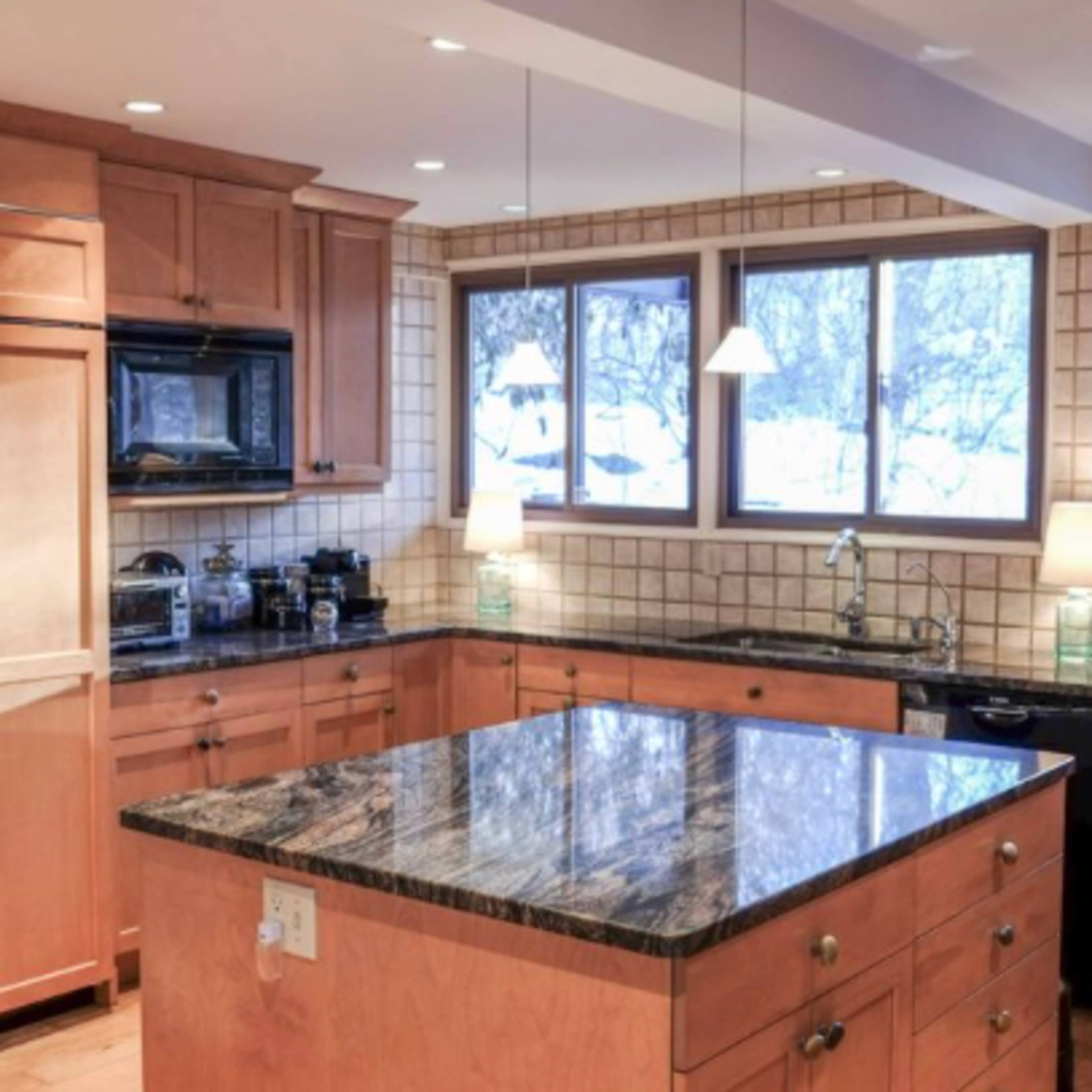 The kitchen features wooden cabinetry, a large island with a dark granite countertop, and multiple windows providing natural light.