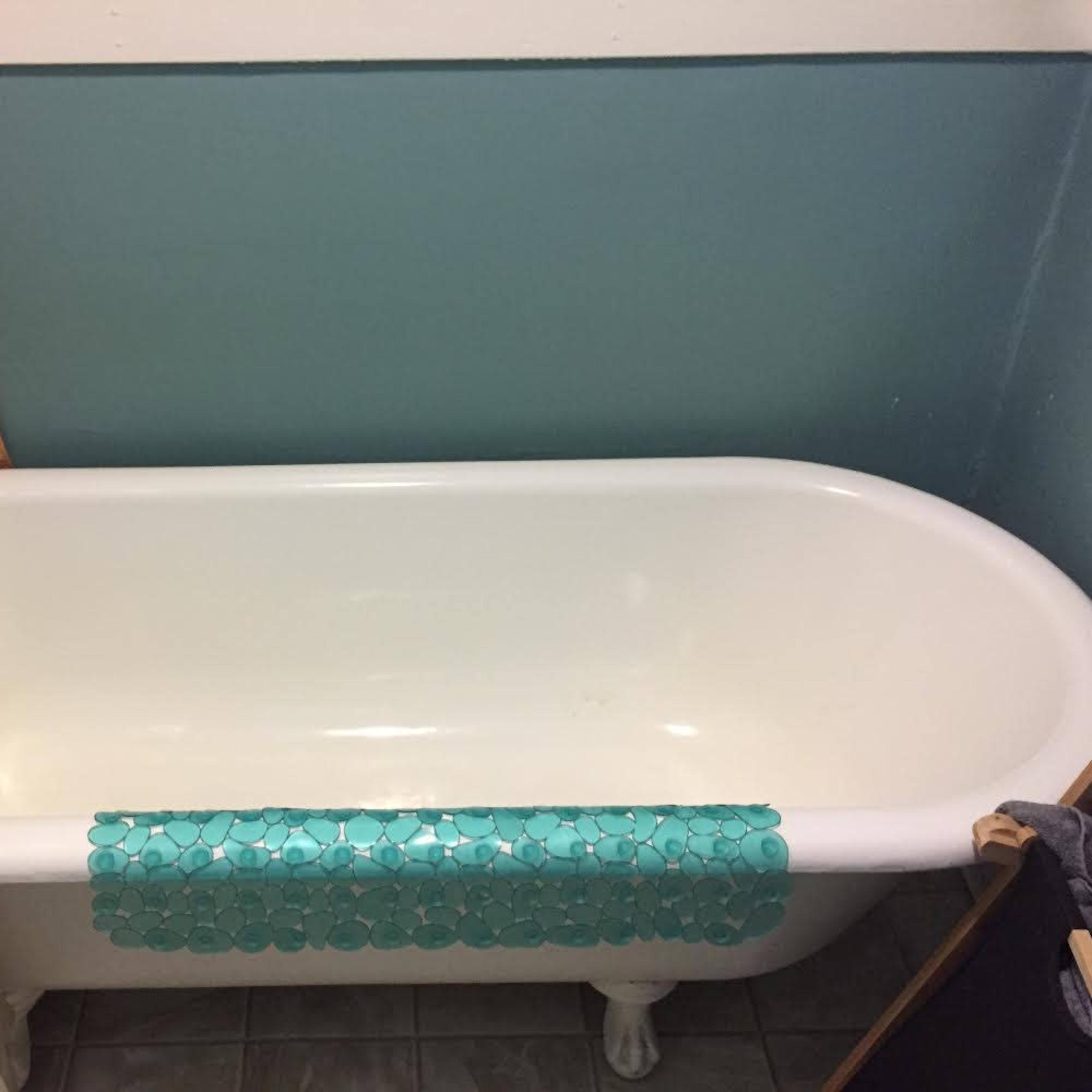 A white bathtub with decorative blue tiles placed along the edge, situated in a bathroom with a colorful curtain and turquoise wall.