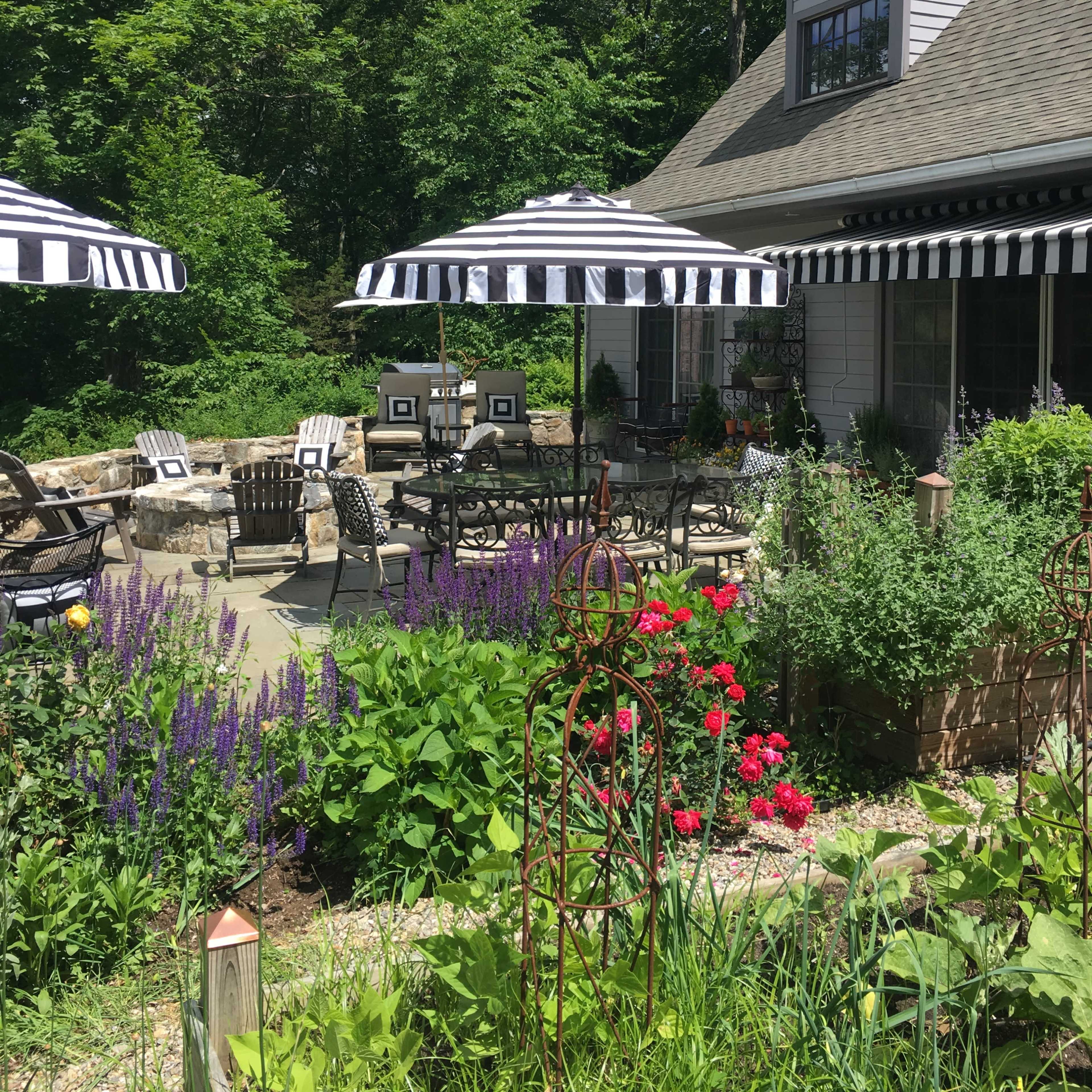 A patio area with striped umbrellas surrounded by blooming flowers and greenery in a residential garden.