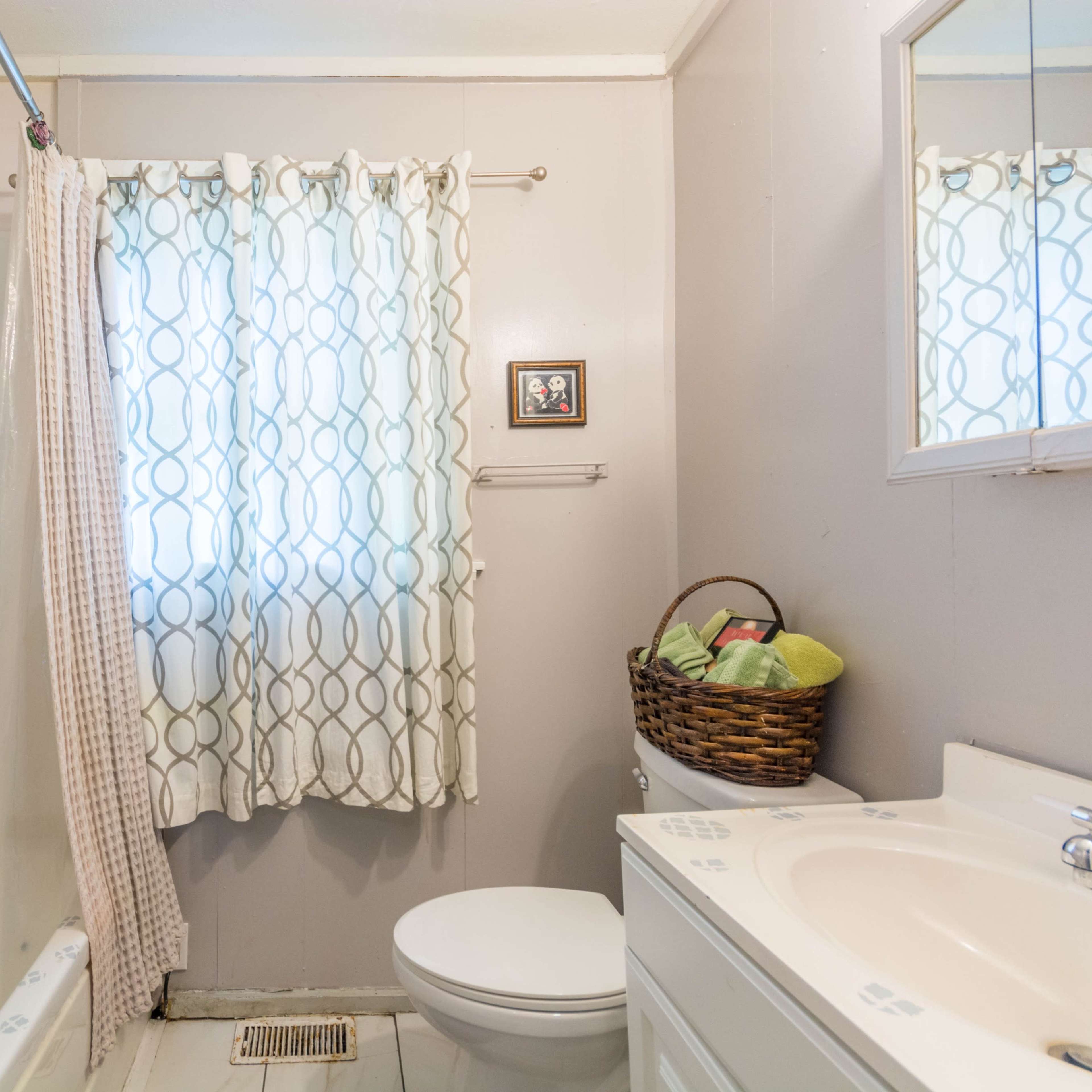 A small bathroom featuring a bathtub with a shower curtain, a toilet, a sink with a mirror, and a basket containing towels.