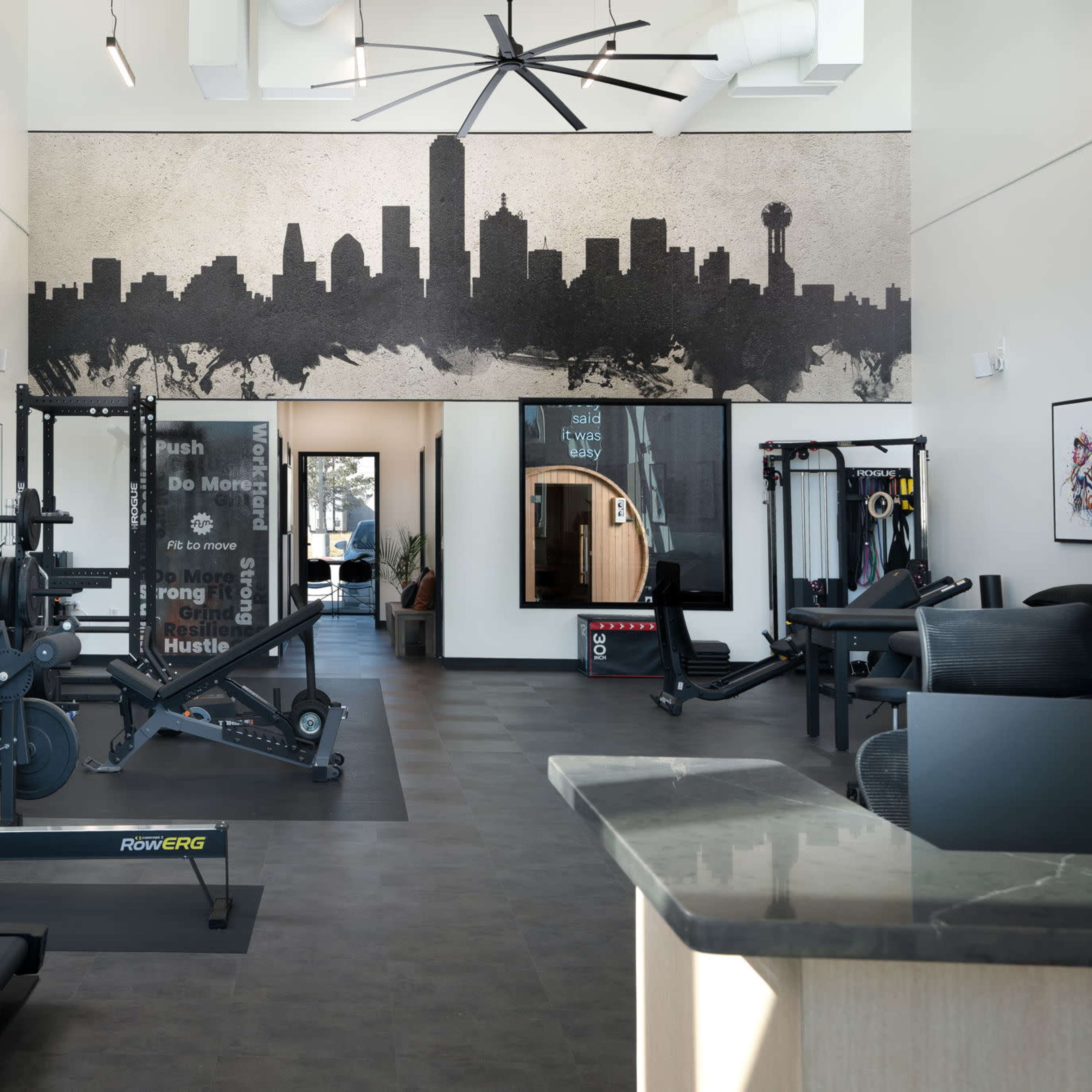 A modern gym interior featuring various exercise equipment, a large wall mural of a city skyline, and ample natural light.