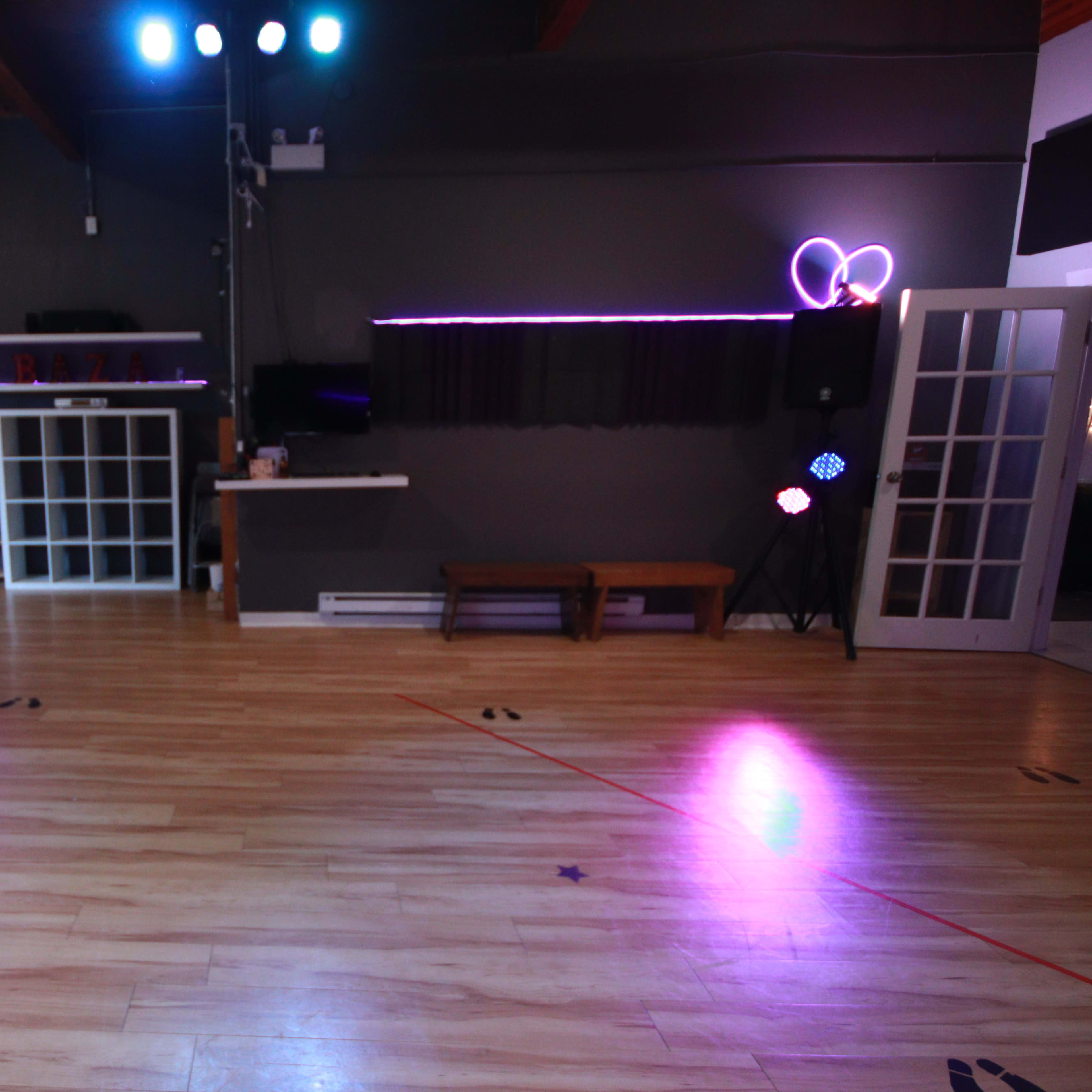 An empty dance studio with wooden floors, colored stage lights, and a mirrored wall.
