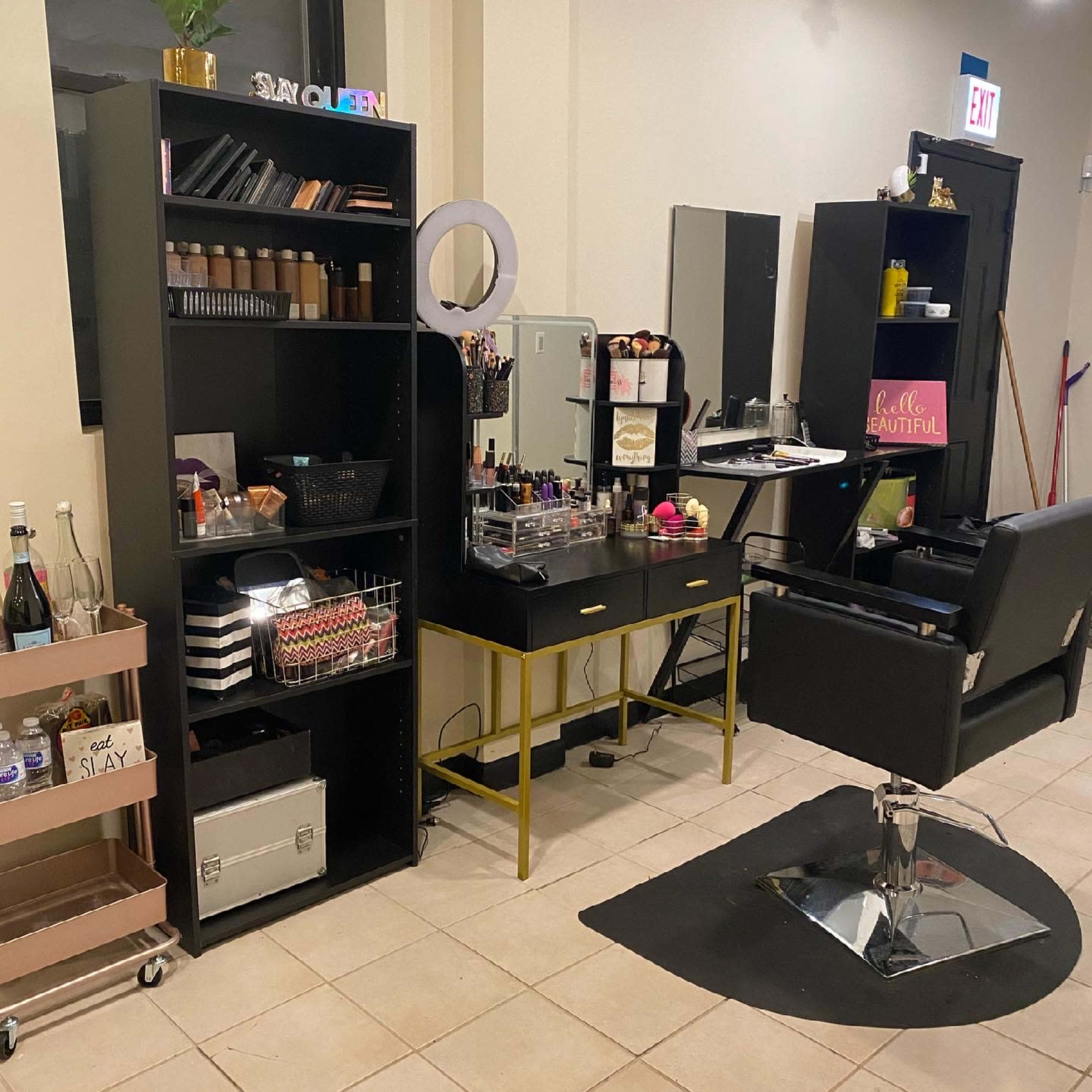 A makeup station with black shelving units, a mirror, and a chair, all set up in a well-lit room.