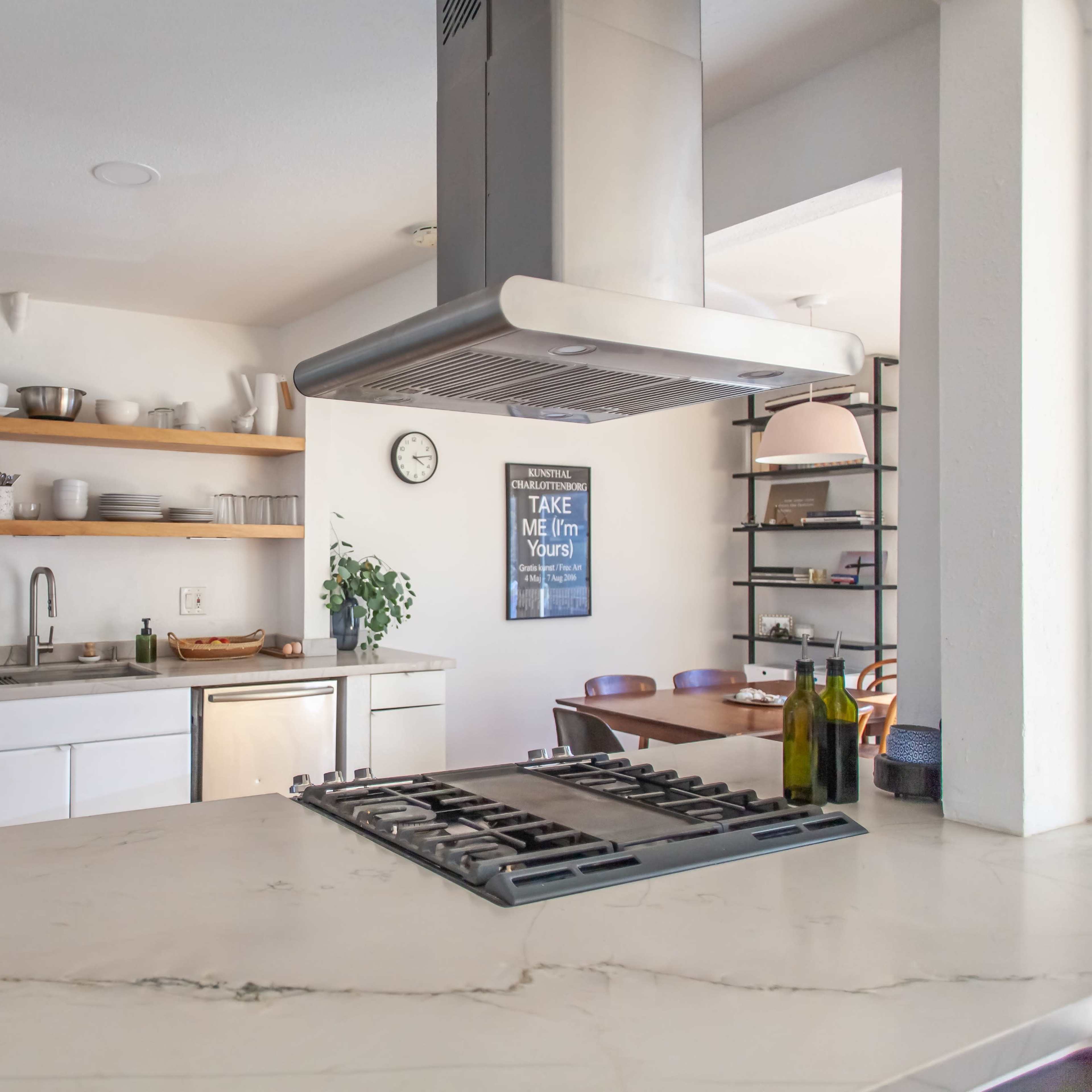A modern kitchen features stainless steel appliances, open shelving, and a gas stove with a large hood.