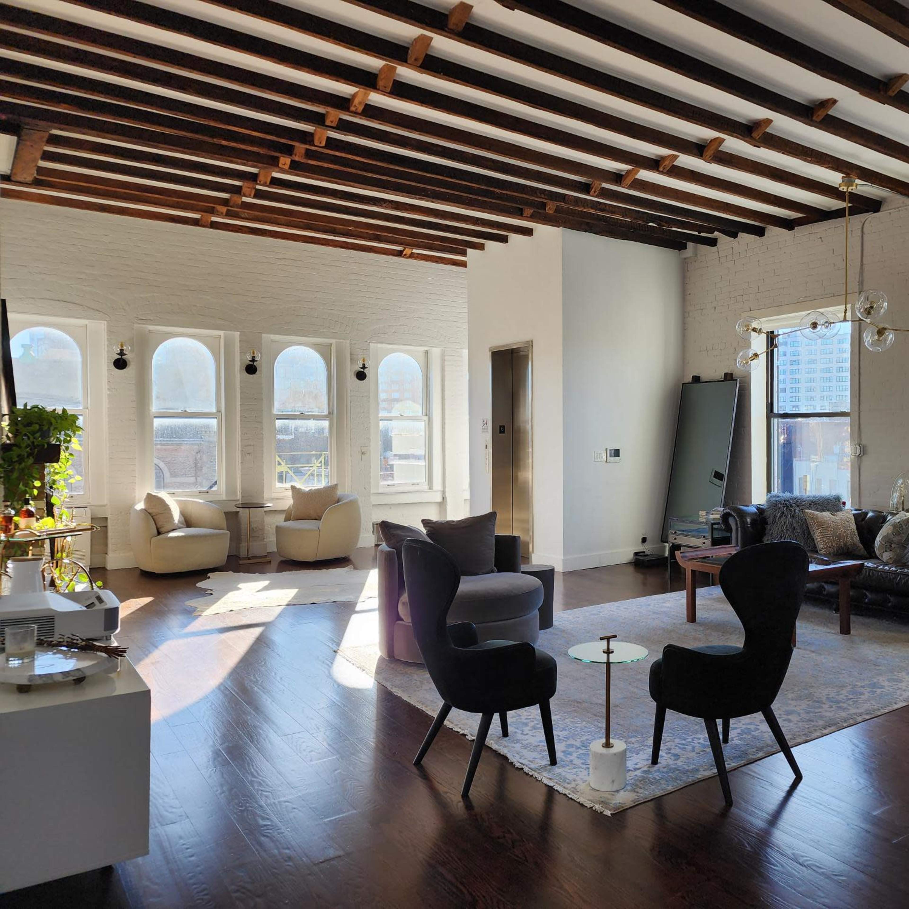 A spacious living room features modern furniture, large windows, and exposed wooden beams on the ceiling.
