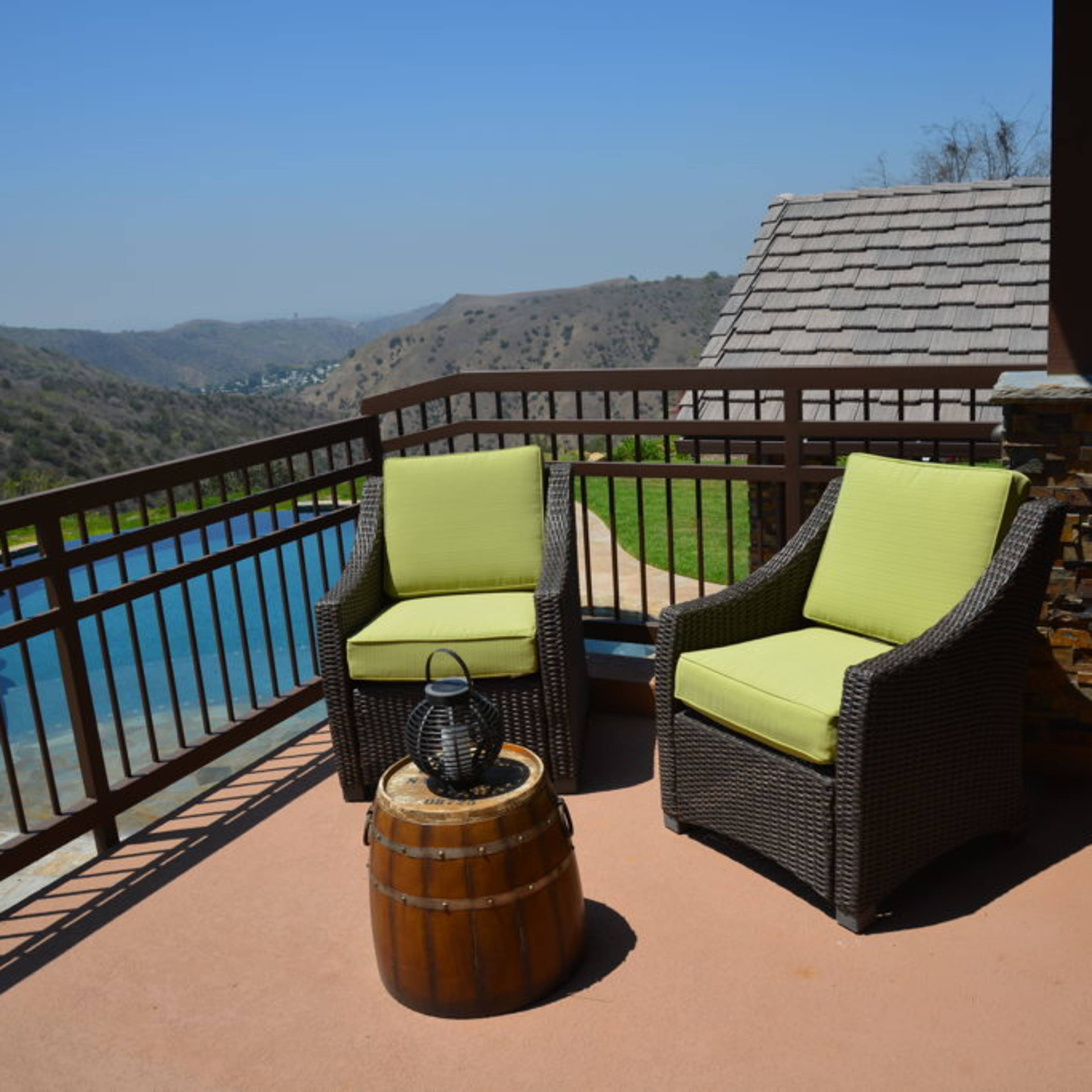 A pair of lime green chairs sit beside a wooden barrel on a balcony overlooking a pool and hillside landscape.