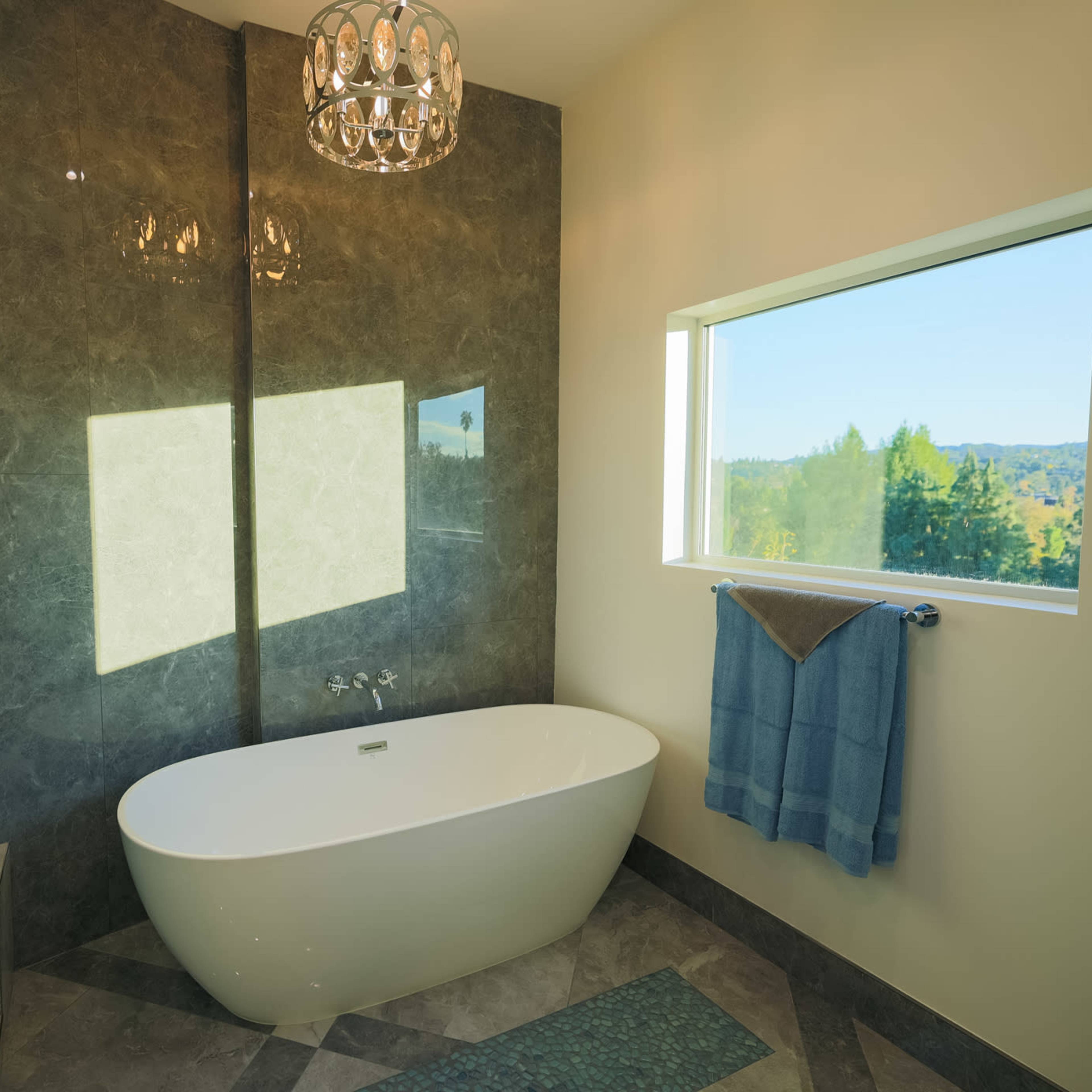 A modern bathroom features a freestanding bathtub beside a window with a view of the landscape, illuminated by natural light.