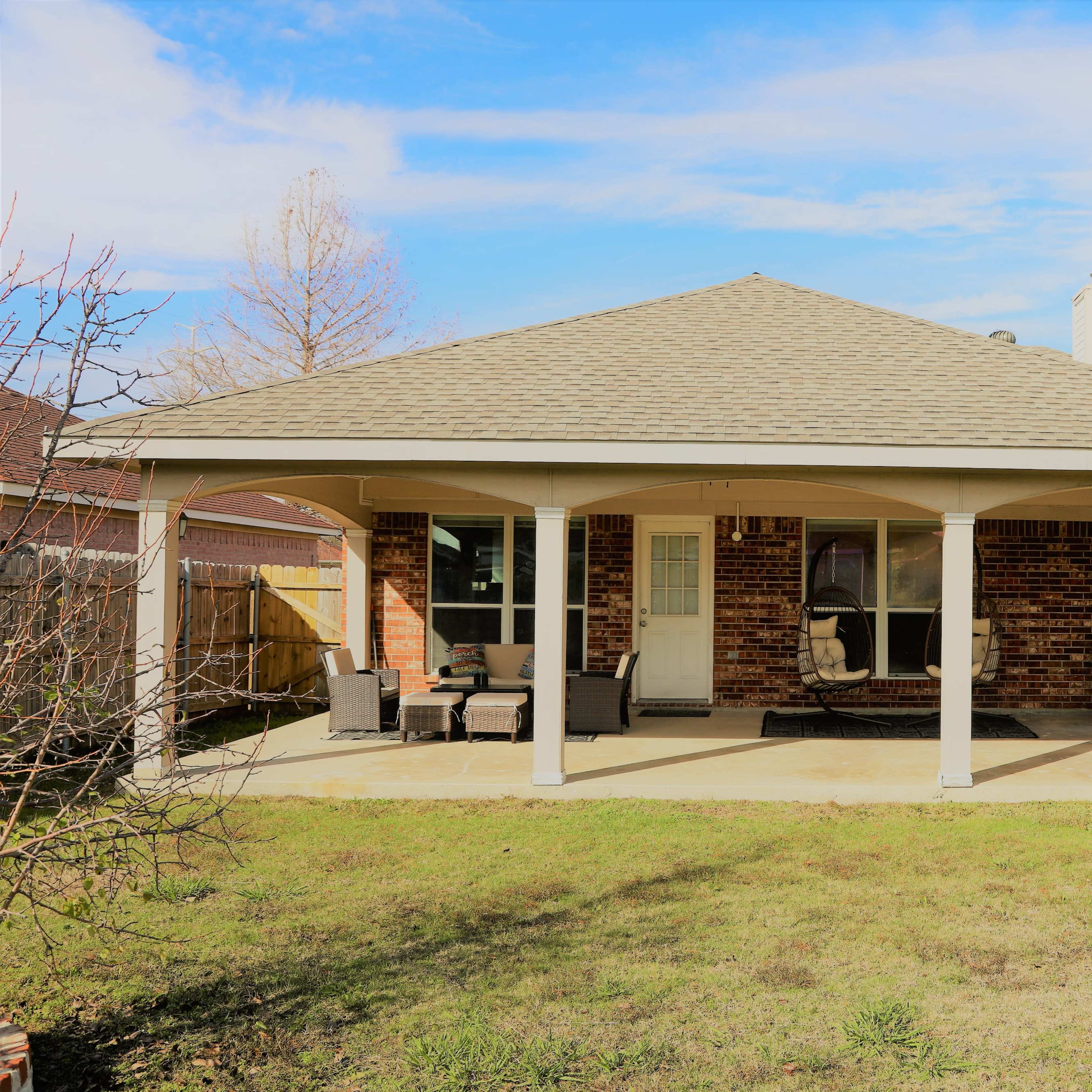 A brick house with a covered patio and outdoor seating area surrounded by grass.