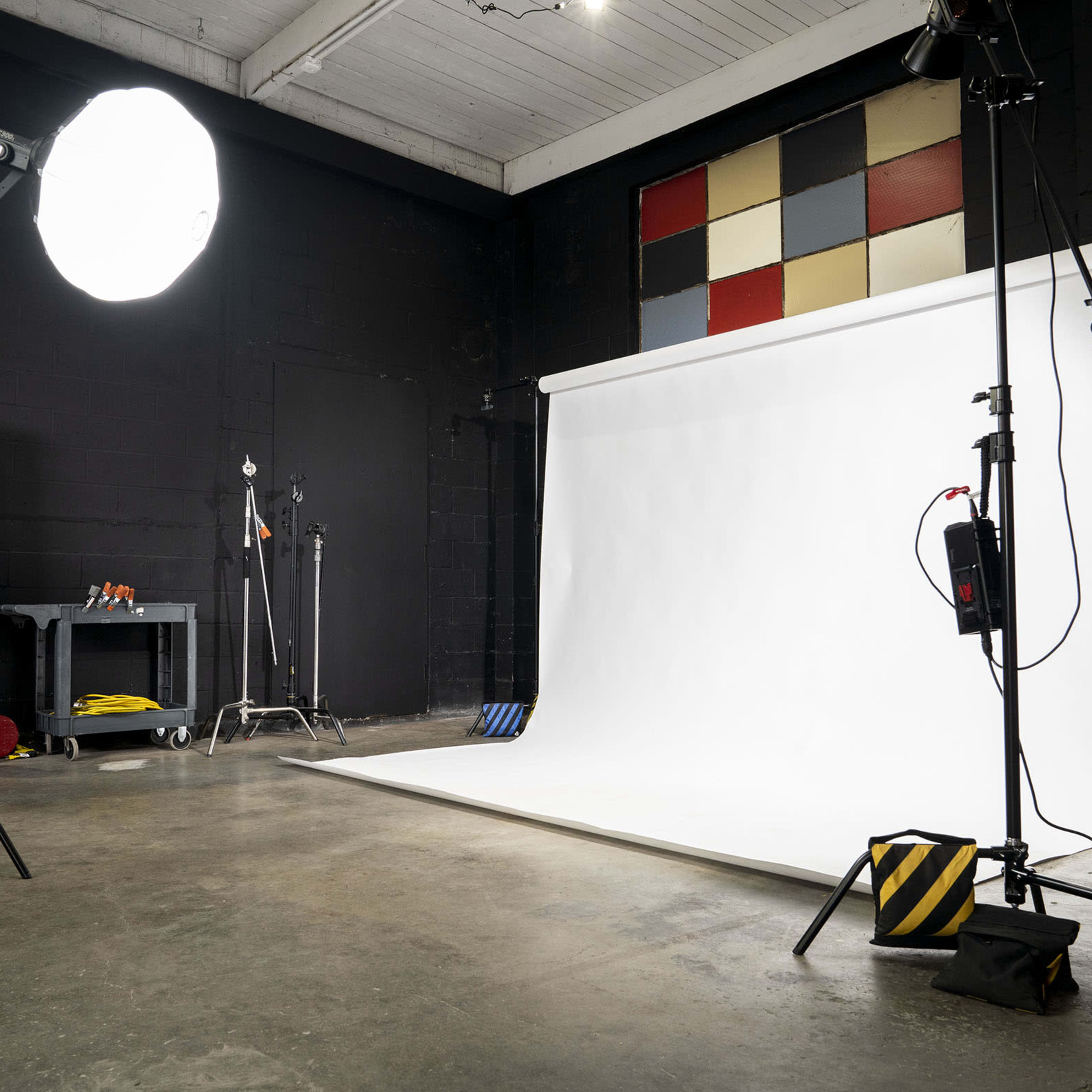 A photography studio with a white backdrop, lighting equipment, and a concrete floor.