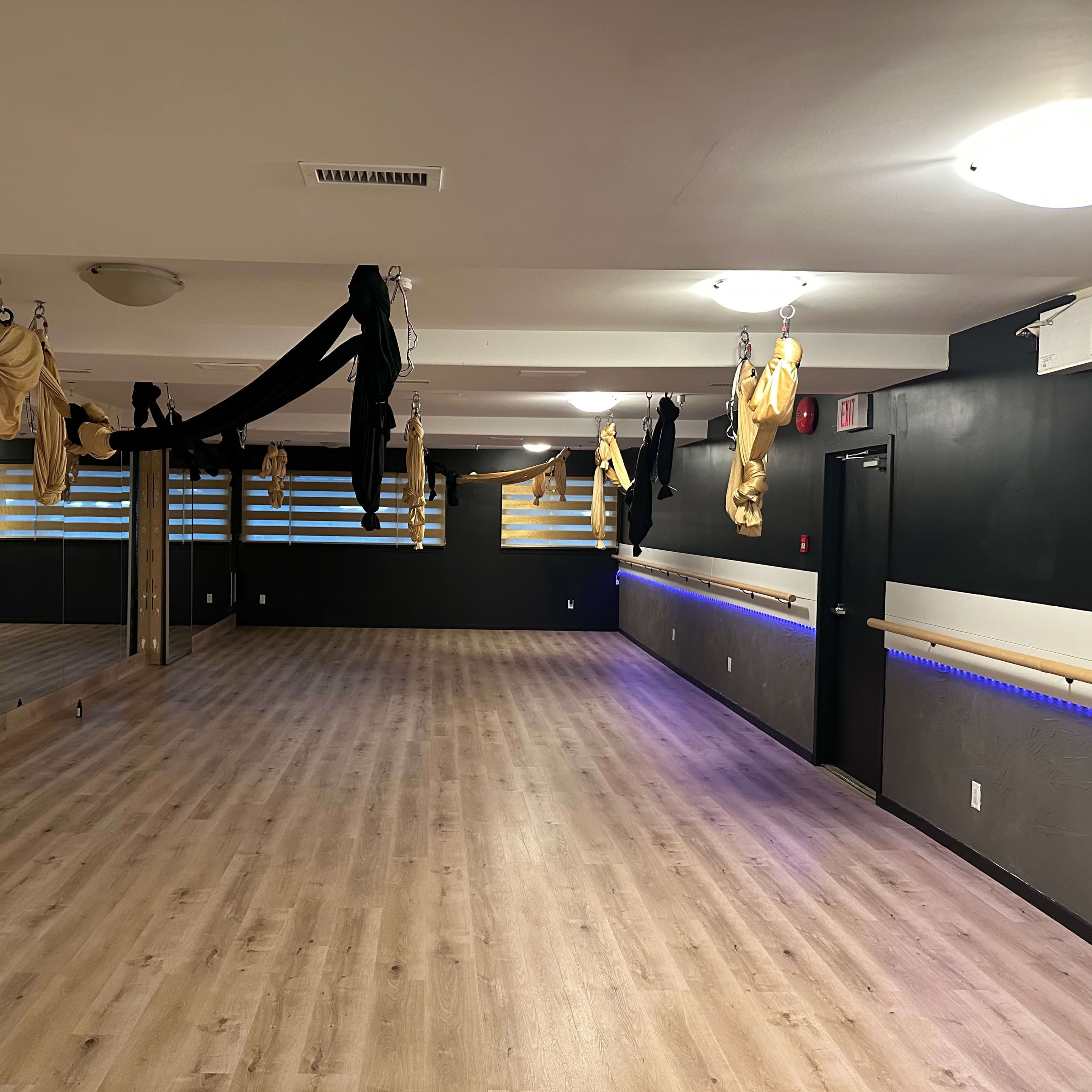 An empty gym studio with mirrored walls and suspended fabric hanging from the ceiling.