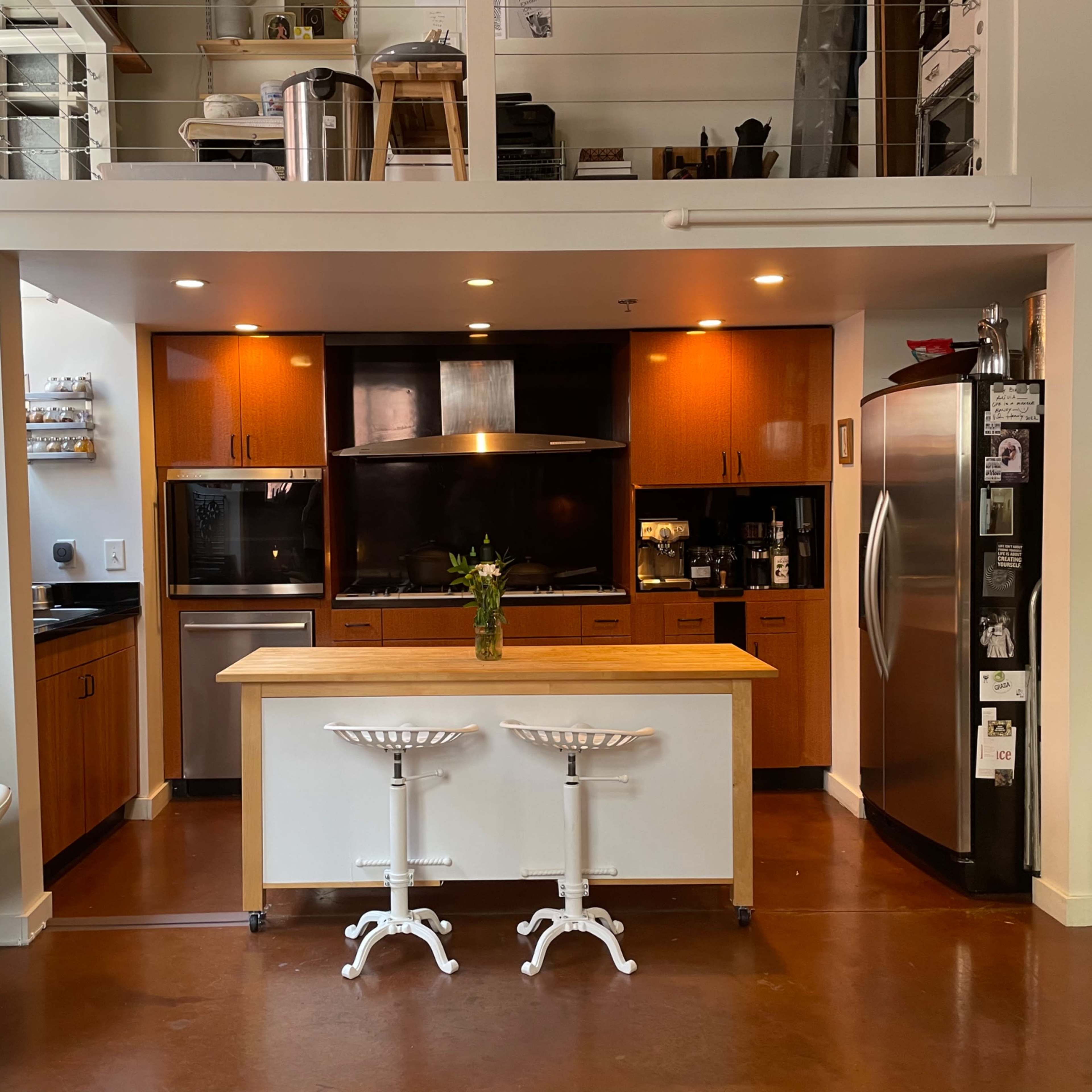 A modern kitchen features wooden cabinetry, stainless steel appliances, and a central island with two bar stools.