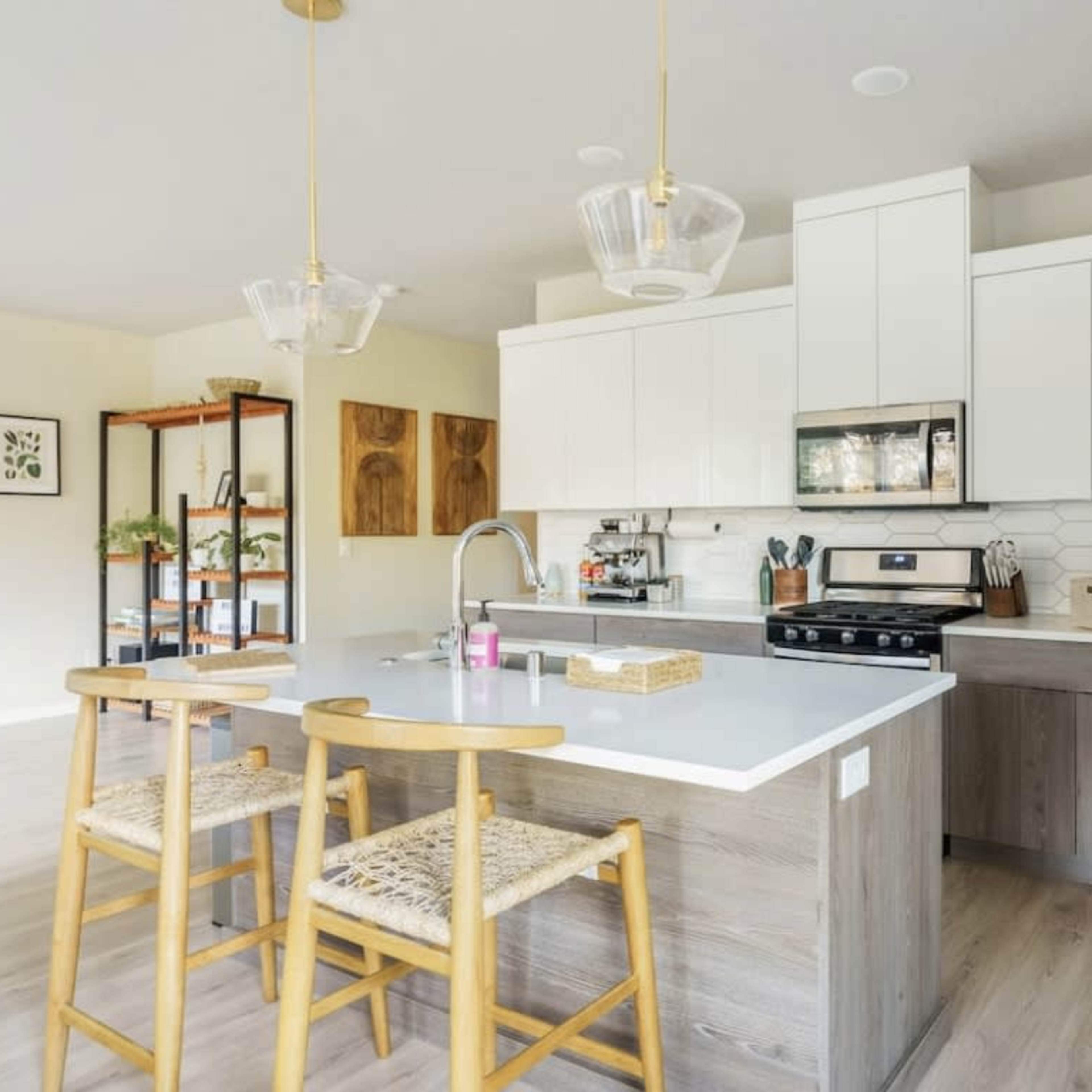 A modern kitchen features white cabinetry, a gray countertop, and wooden barstools, providing a clean and functional space.