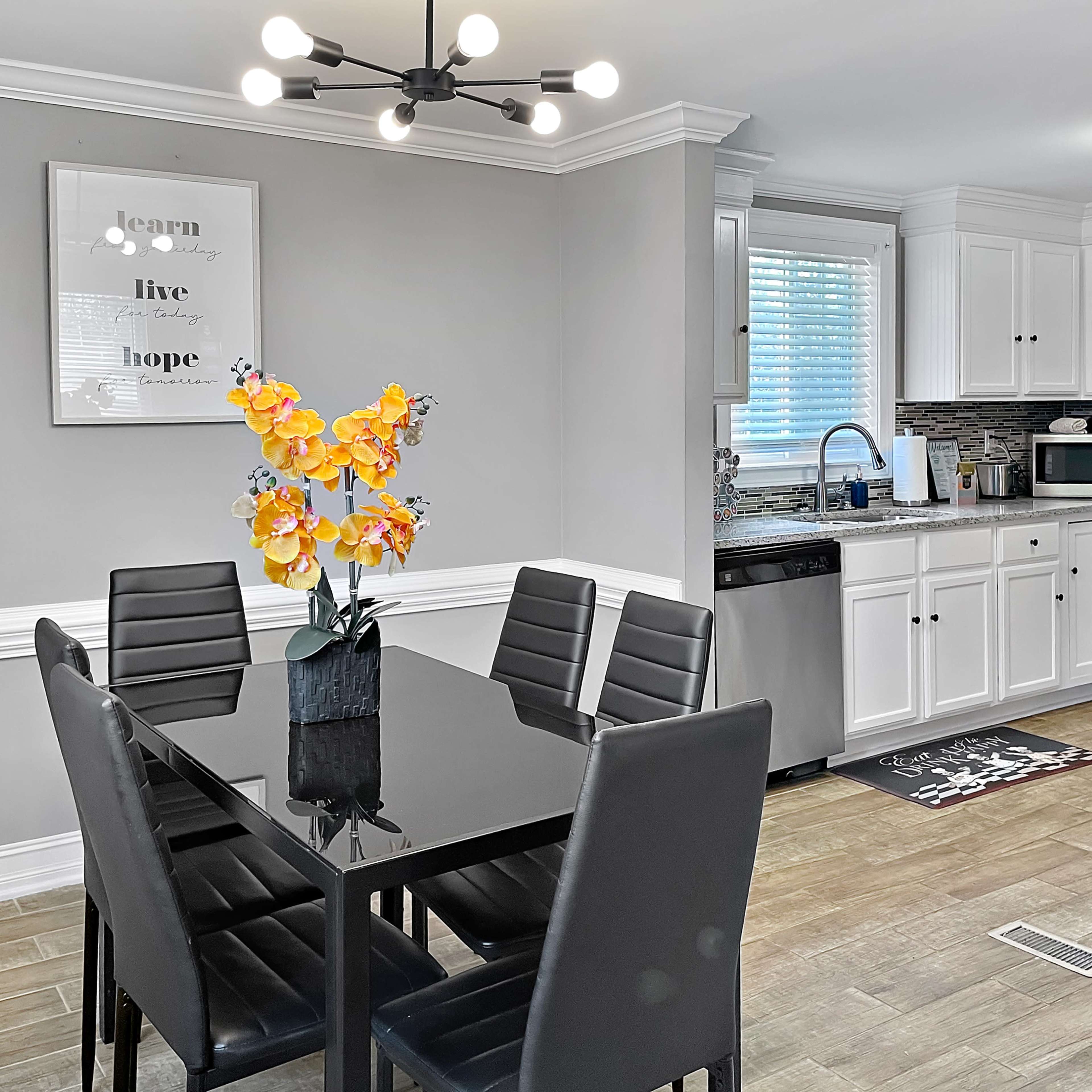 A modern kitchen features a dining area with a black table and chairs, surrounded by white cabinets and stainless steel appliances.