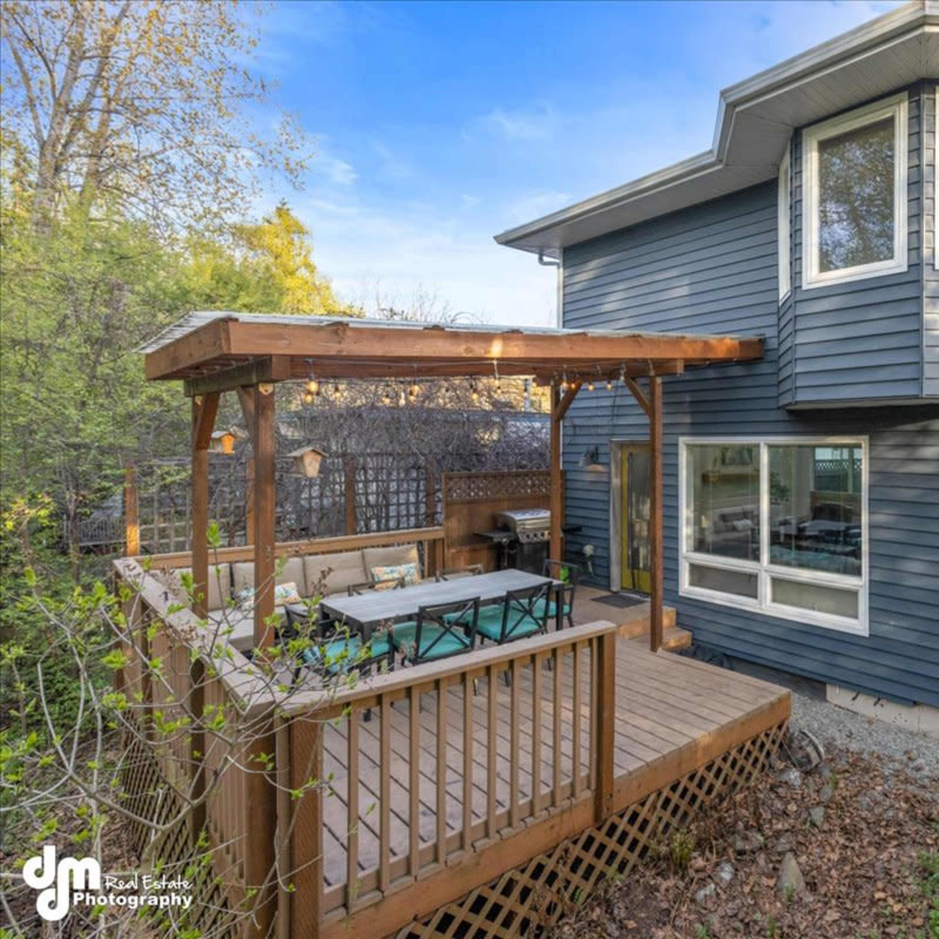 A modern two-story house with blue siding, featuring a wooden deck with outdoor seating and a pergola.