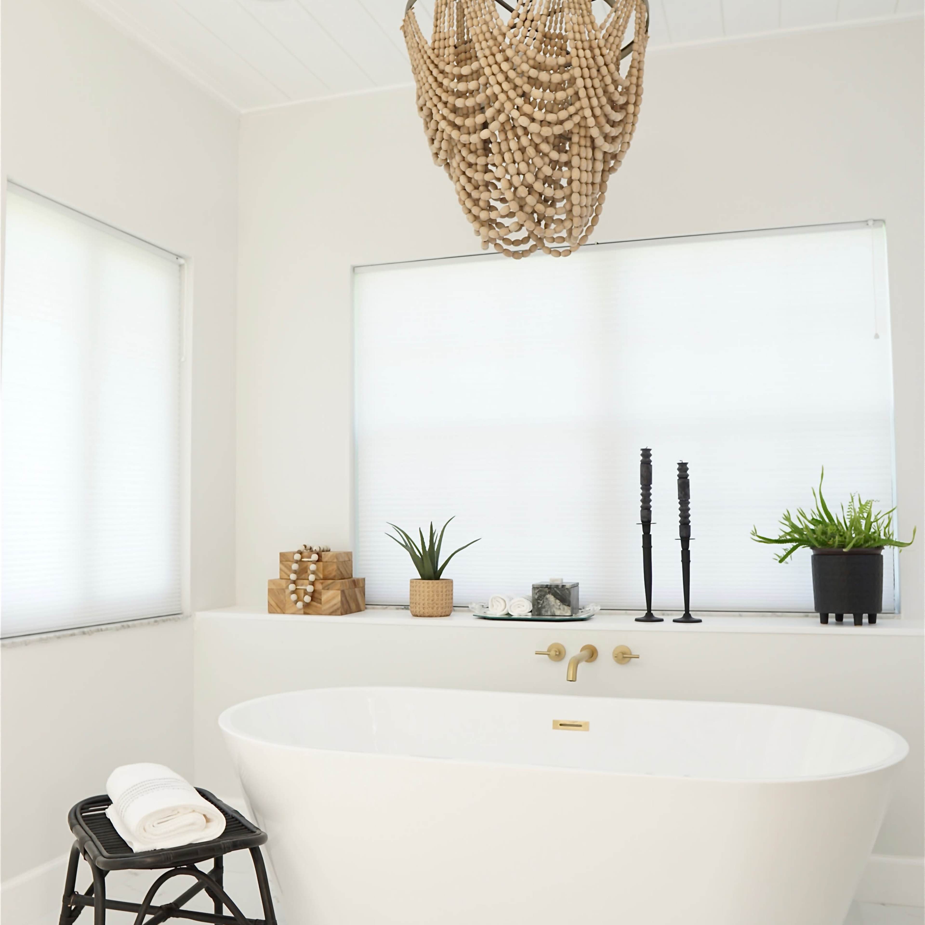 A modern bathroom features a freestanding white tub, a decorative beaded chandelier, and potted plants on a minimalist countertop.