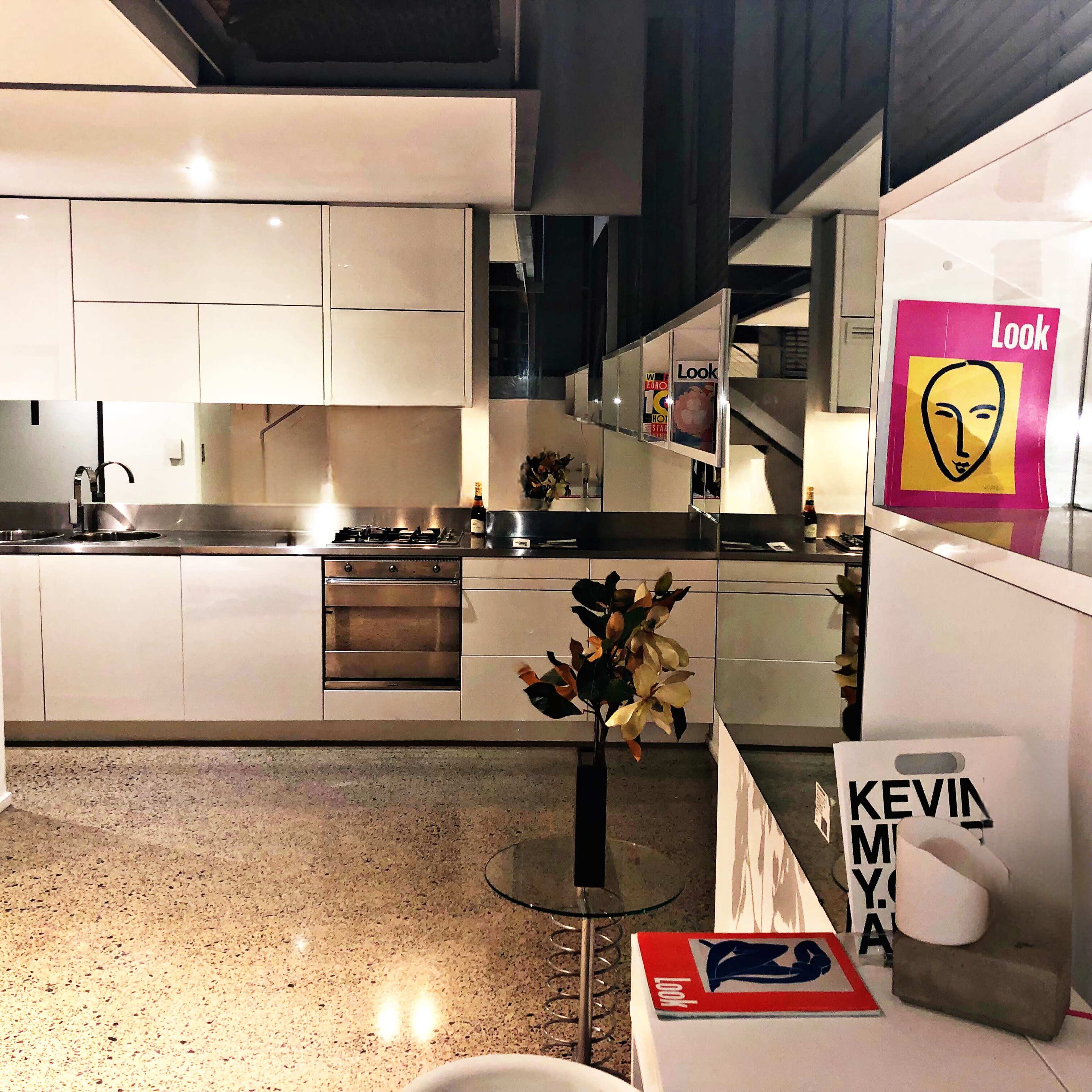 A modern kitchen features sleek white cabinetry, stainless steel appliances, and decor items, with a mirror reflecting the space.