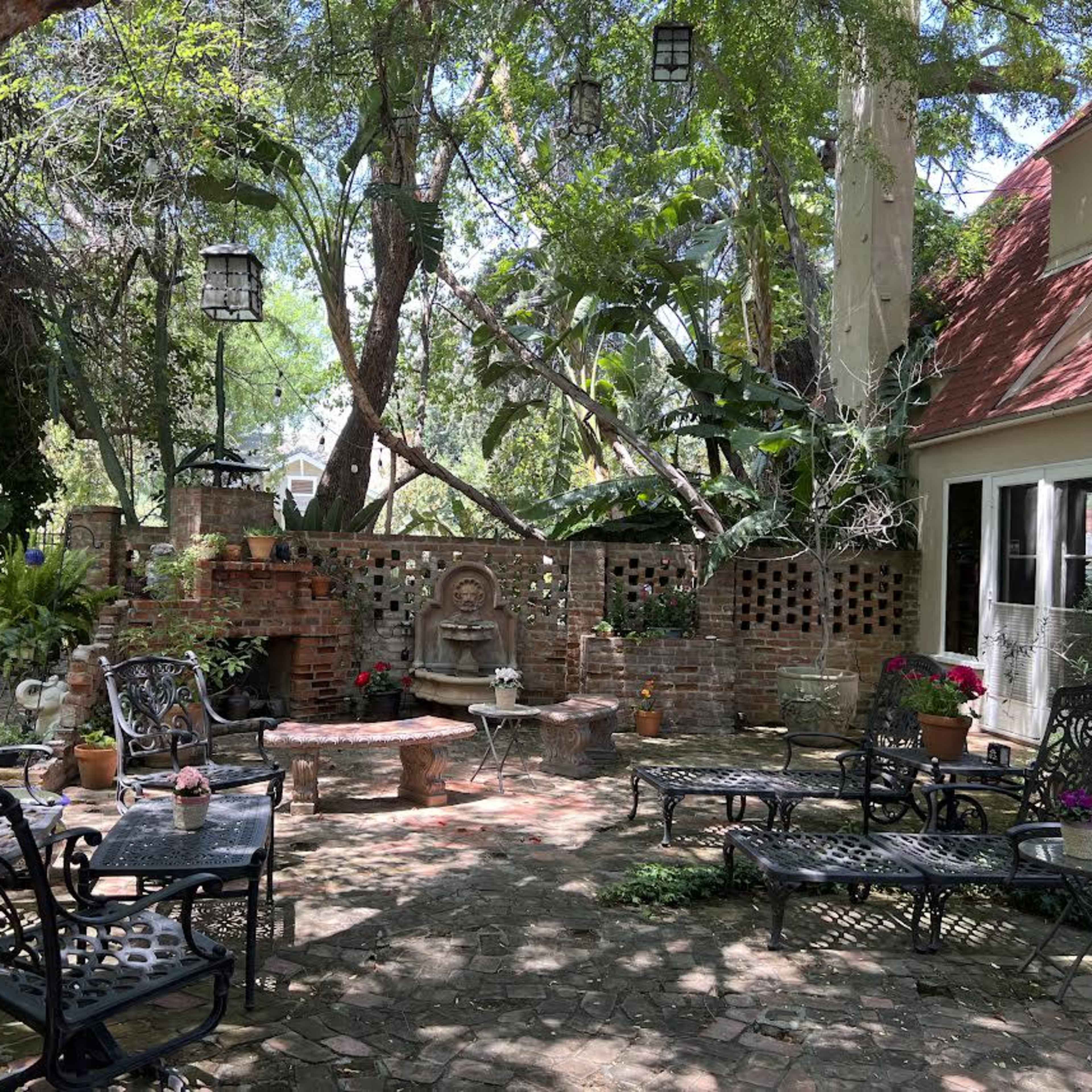 A tranquil courtyard with stone pathways, decorative seating, and lush greenery surrounding a central fountain.