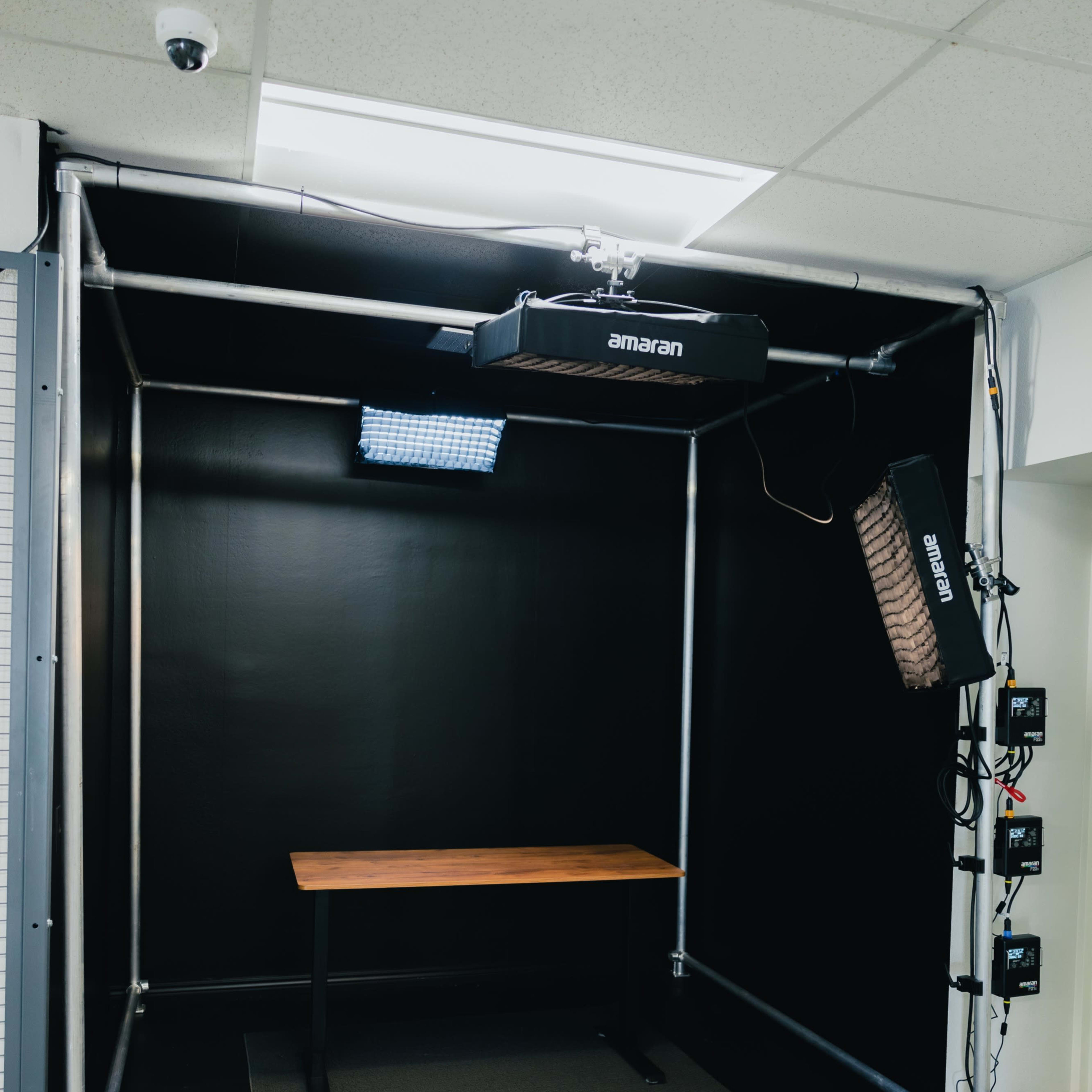 A photography studio with a black backdrop, a wooden table in the center, and positioned lighting equipment.