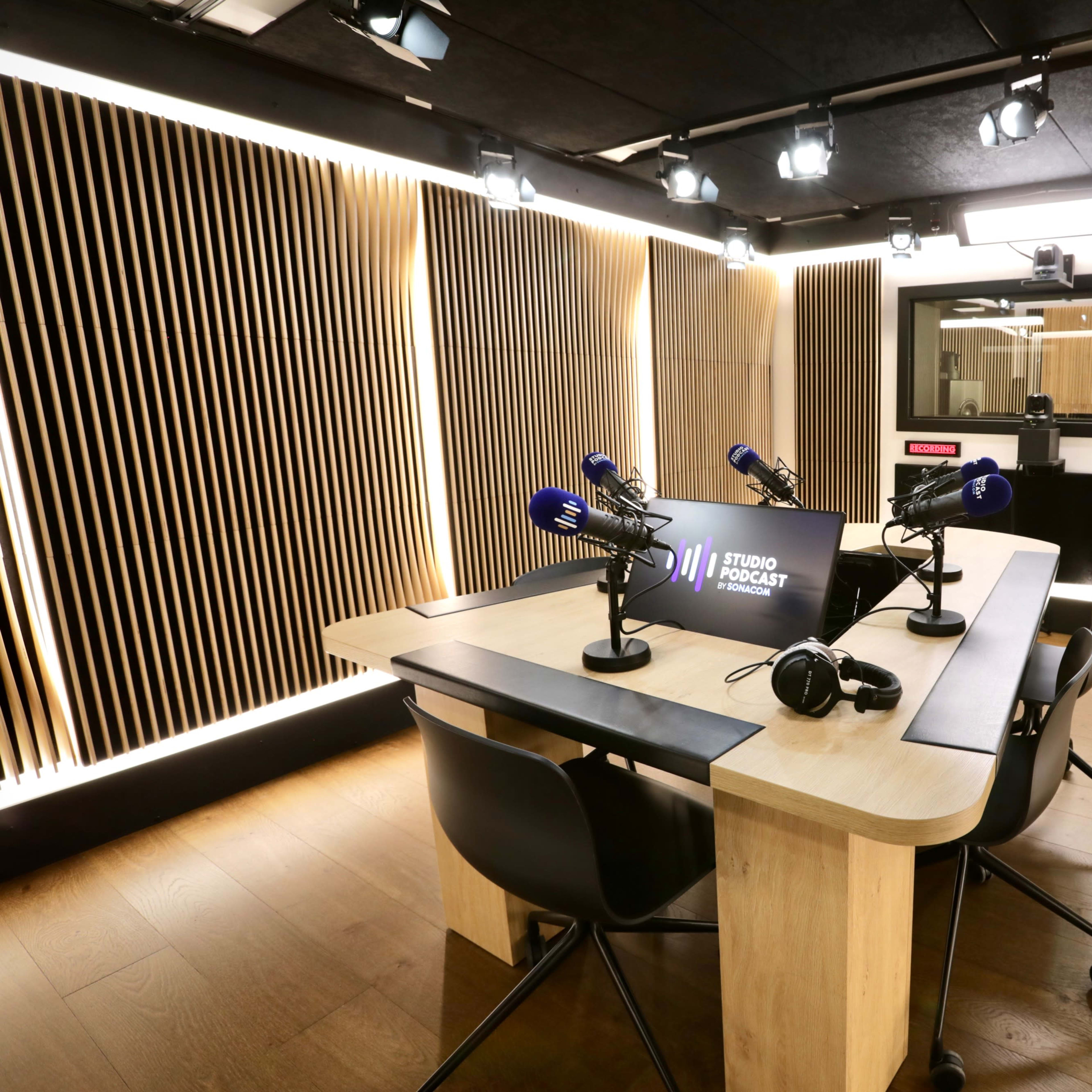A modern podcast studio featuring a wooden table, multiple microphones, and adjustable lighting.