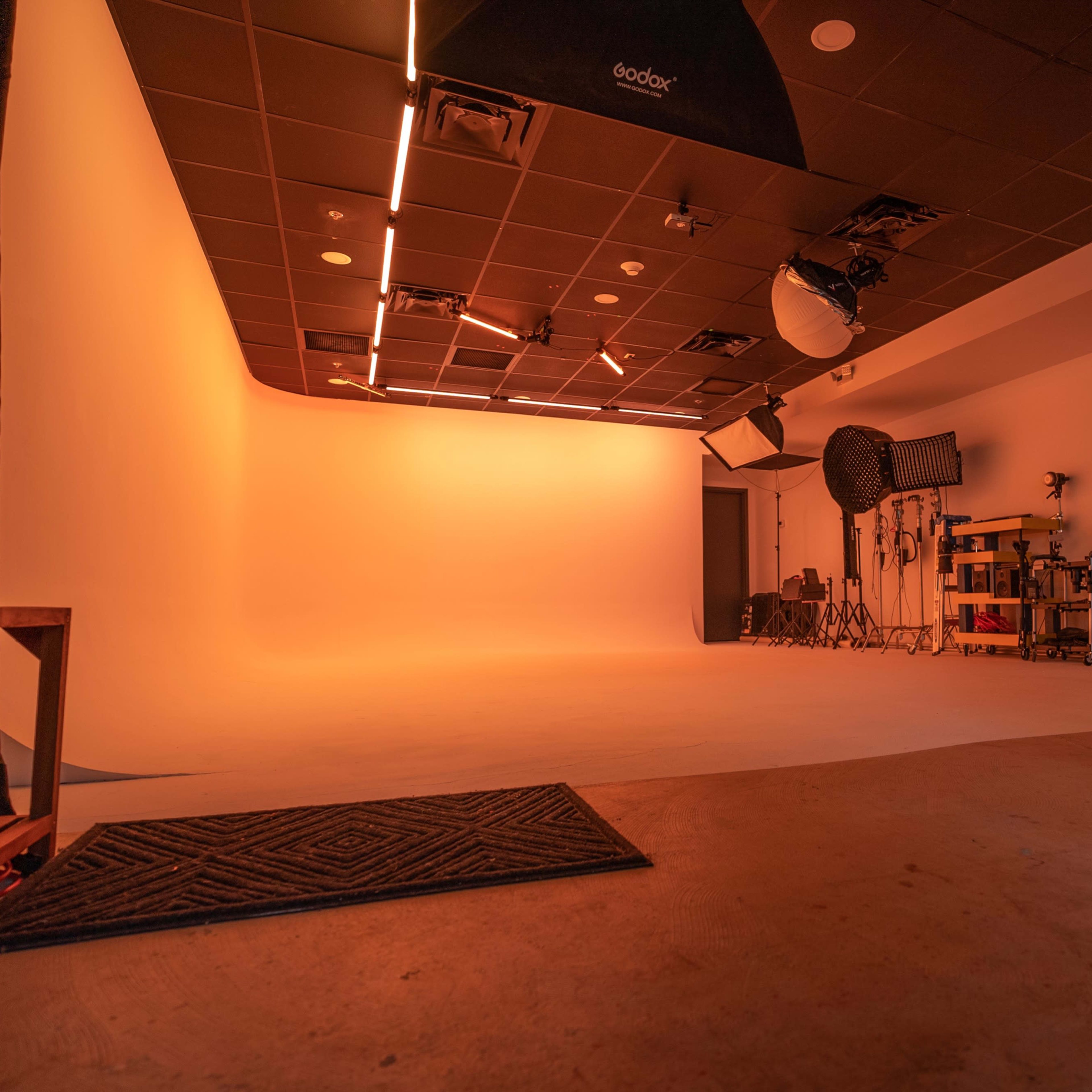 An empty photography studio with an orange-lit backdrop and various photographic equipment arranged against the walls.