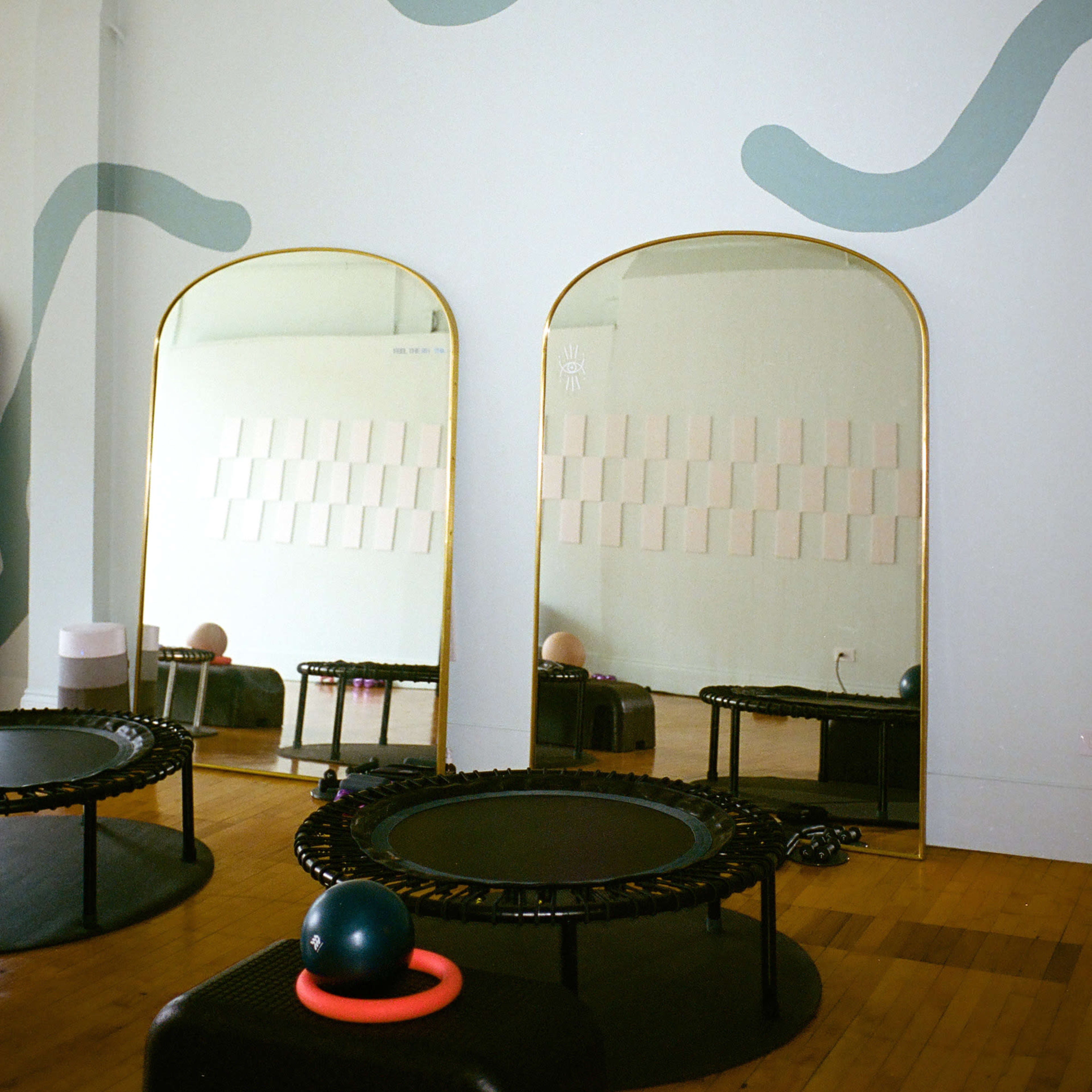 A room with three trampolines and two large mirrors featuring curved wall designs and pastel-colored tiles.